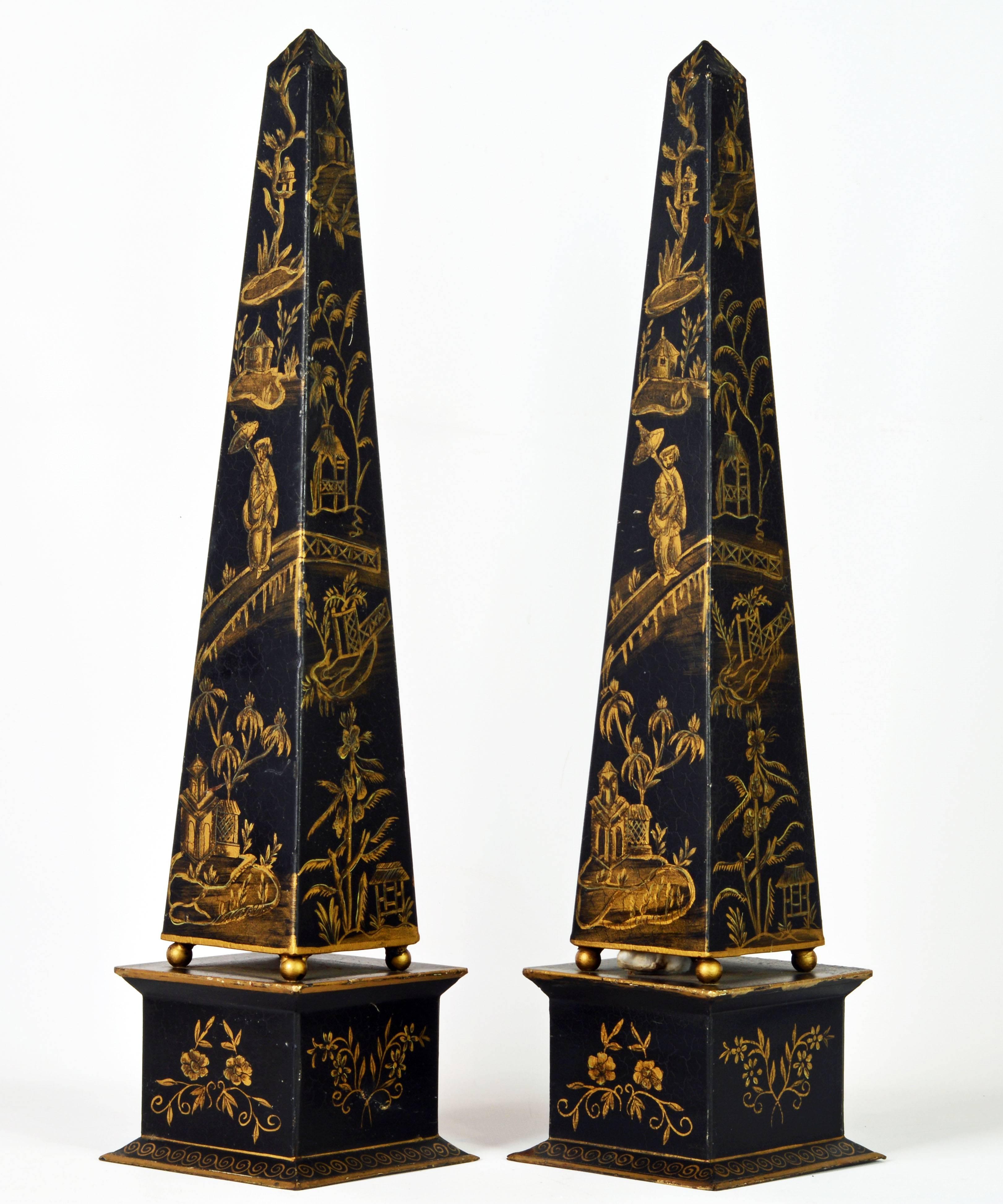 Standing almost 22 inches tall this charming pair of Brighton Pavilion era tole obelisks are painted in black and gold with chinoiserie motifs from top to bottom intersected by decorative borders. The obelisks are classically fashioned with an upper