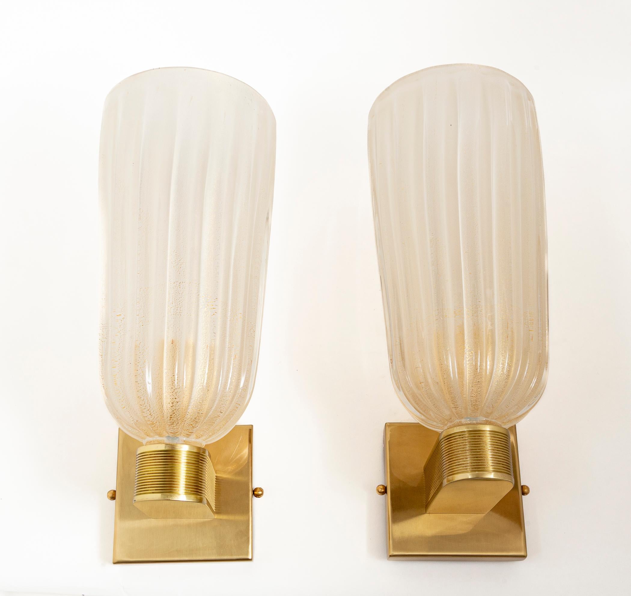 Un elegante par de apliques modernizados de estilo Art Déco, altos y redondos, sostenidos por elegantes brazos acanalados de latón sin lacar.

Cableado con porcelana E26 , listo para instalar con placa trasera de latón de 4,75″ x 4,75″ y certificado