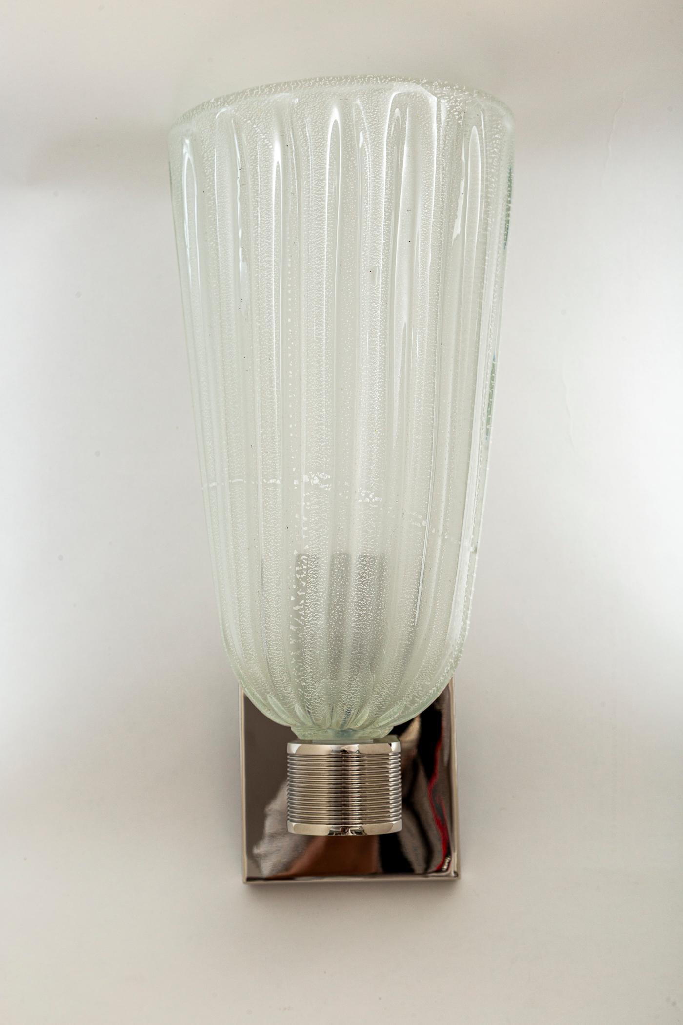 Un'elegante coppia di applique in stile Art&Deco modernizzato, di forma alta e ovale, spesso soffiata con oro bianco su coppe di vetro colorato opaco, sostenute da eleganti bracci a lamelle in nichel lucido.

Cablato con porcellana E26, pronto per