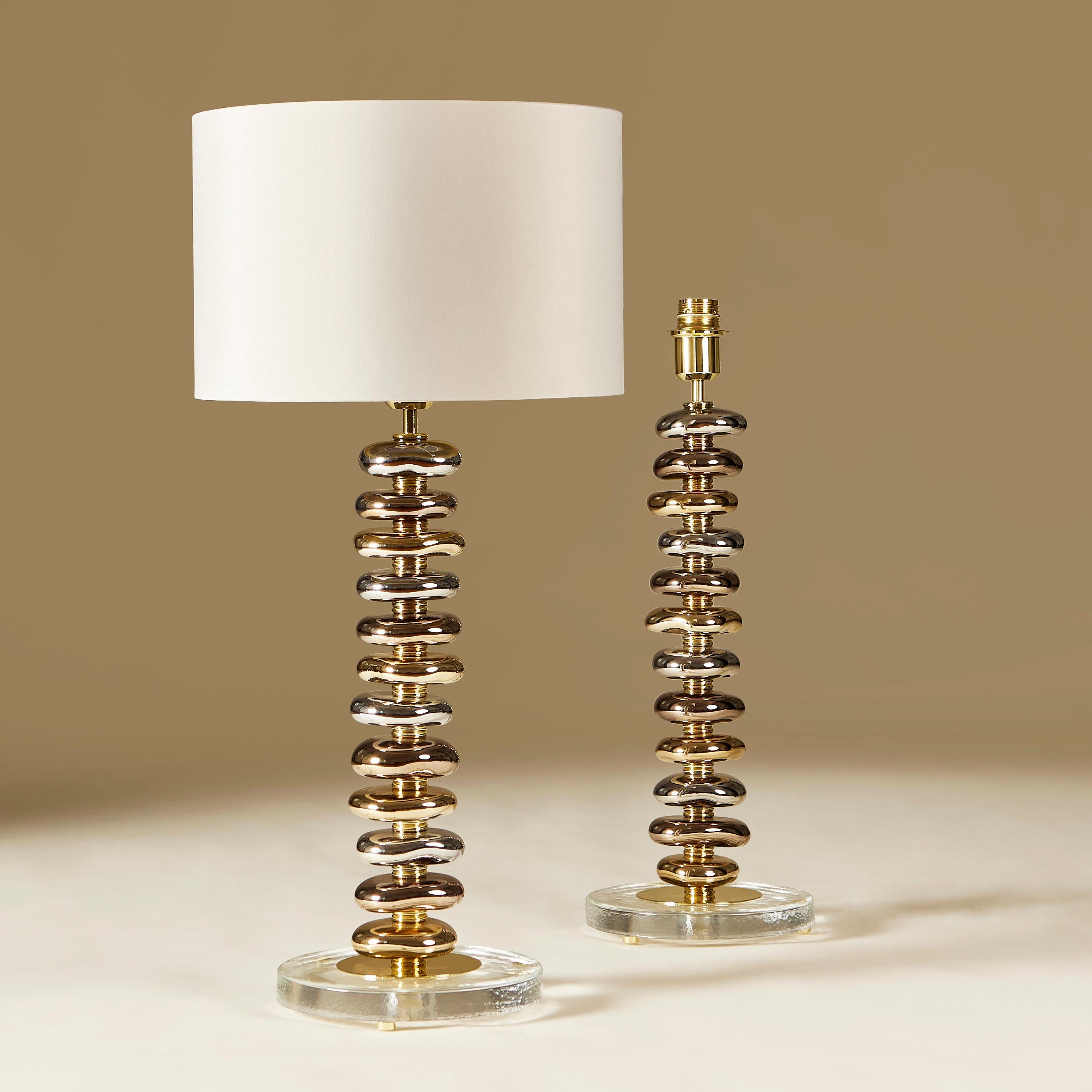 Limited edition pair of contemporary table lamps. Each lamps consists of 12 handmade smooth sculptured Murano pebbles in metallic shades of gold, silver and bronze. Each pebble is interspersed with a tiered layer of brass. Sits on circular glass