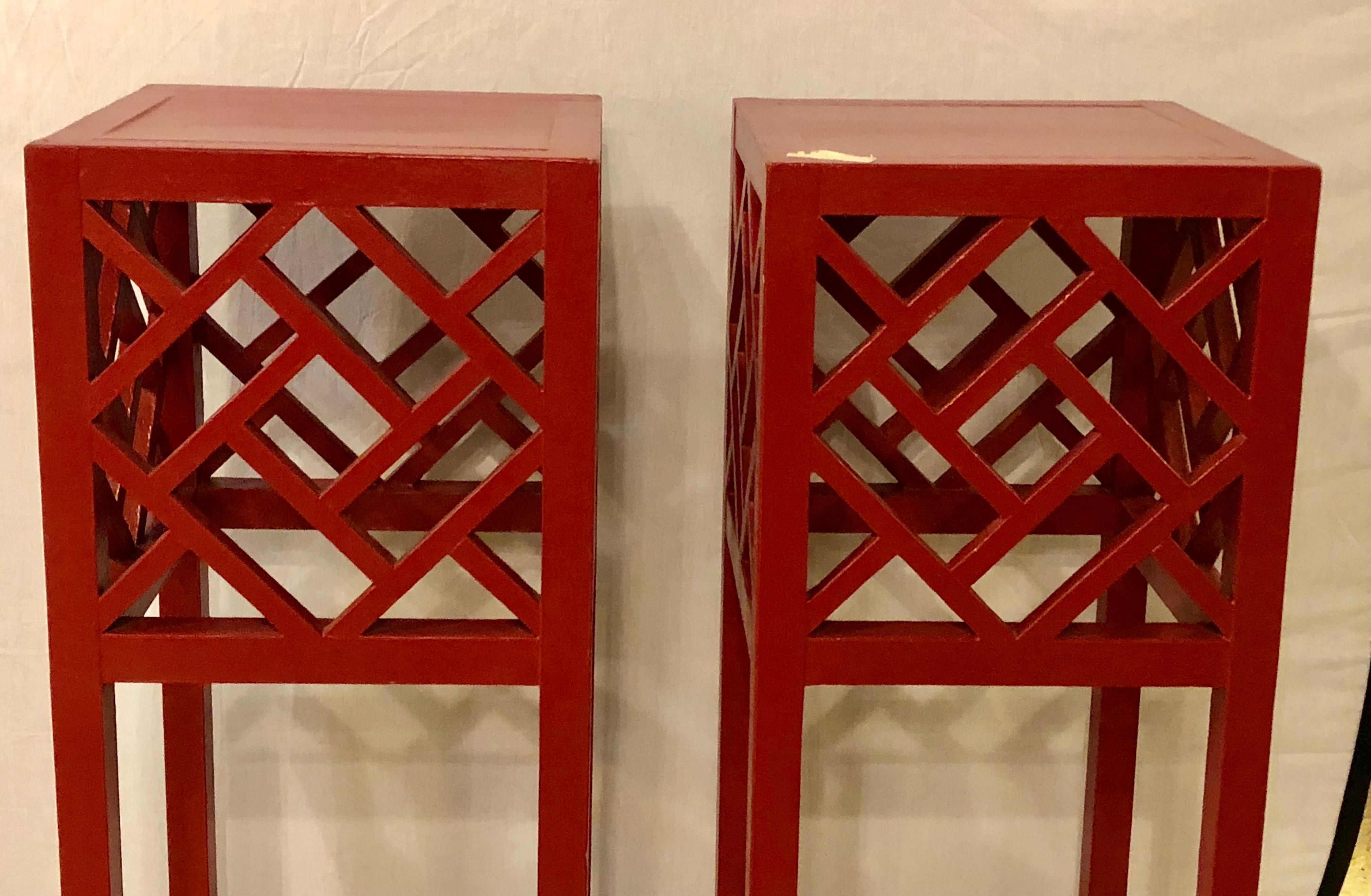 A pair of tall red painted Asian inspired standing pedestals. Sleek and stylish are these finely painted pedestals having a Hollywood Regency X-form design.