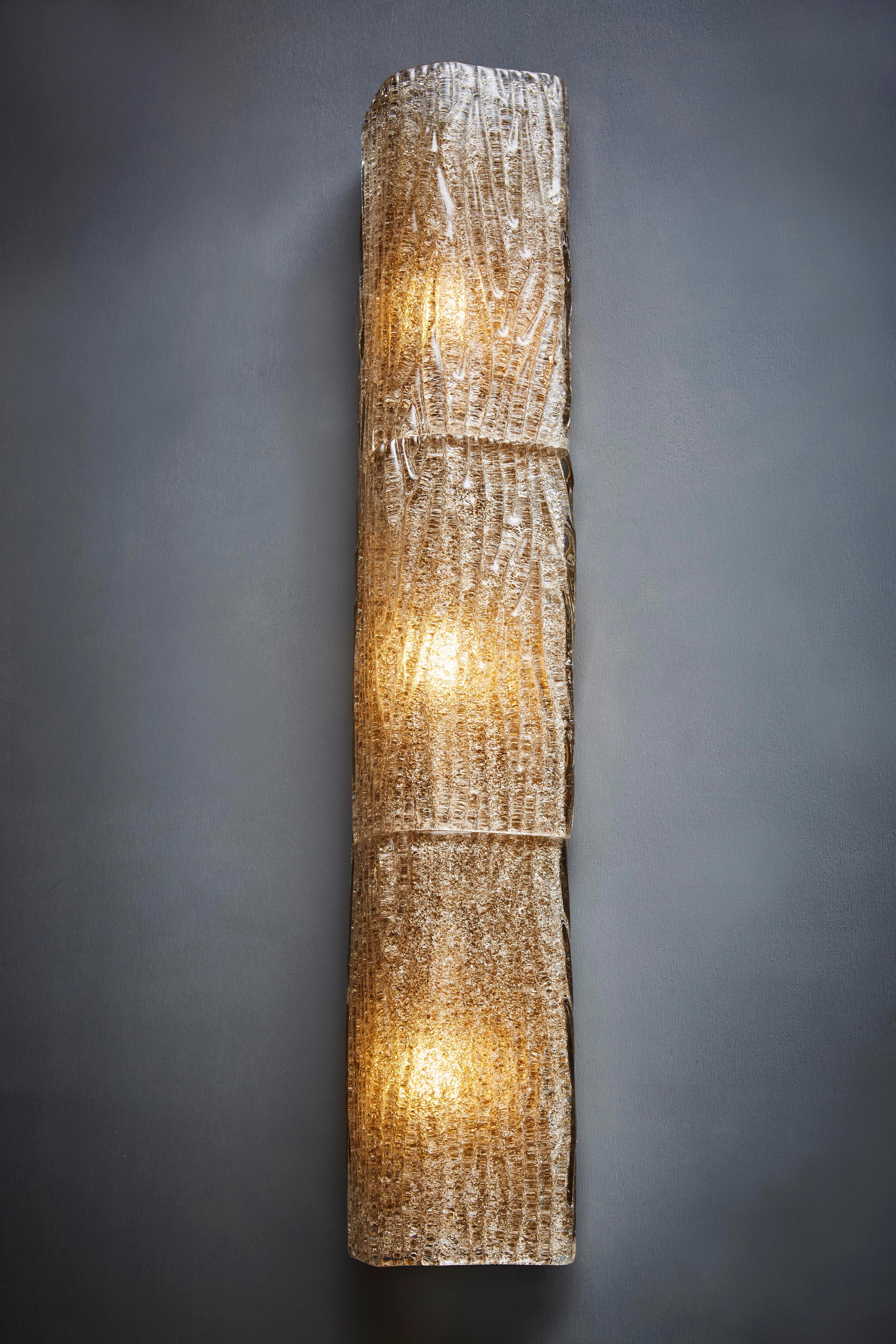 Pareja de apliques altos de latón y tres elementos de cristal de Murano texturado ligeramente tintado y curvado.