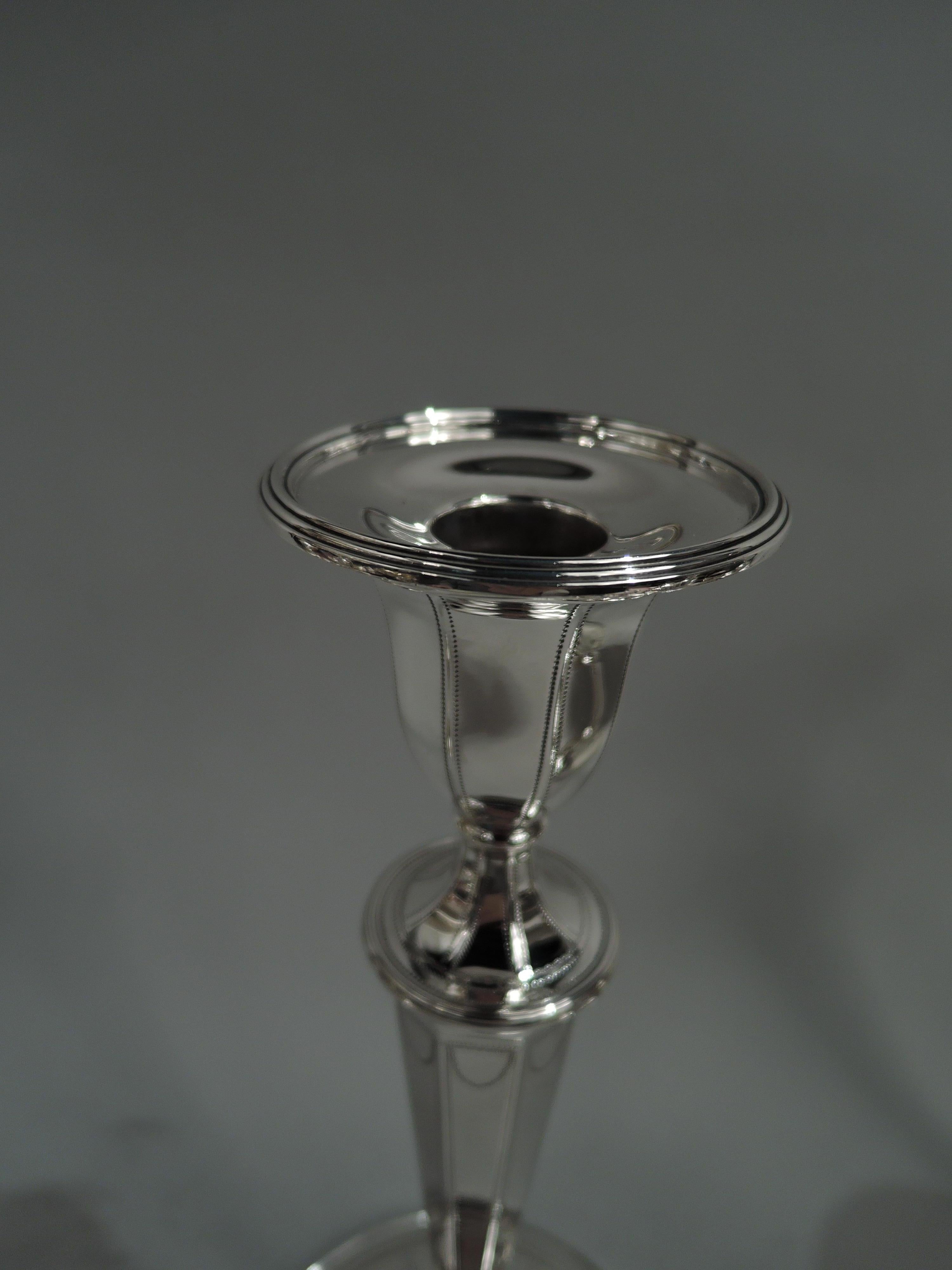 Pair of tall English Neoclassical-style sterling silver candlesticks. Made by Tiffany & Co. in New York, ca 1917. Each: Urn socket with detachable reeded bobeche; tapering shaft on raised and round foot. Pointillé frames and swags and Vitruvian