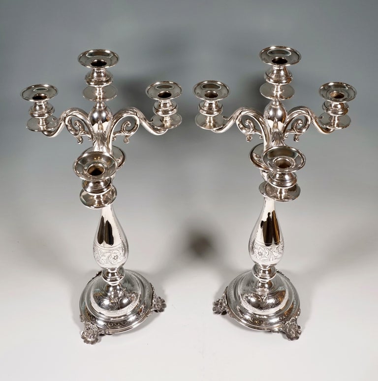 Two four-flame candle holders on a high, cambered foot, raised on three small shell feet, chased flower and leaf tendril decoration on the shaft, three curved volute arms with applied pinnate leaves, bud-shaped spouts with smooth draining discs,