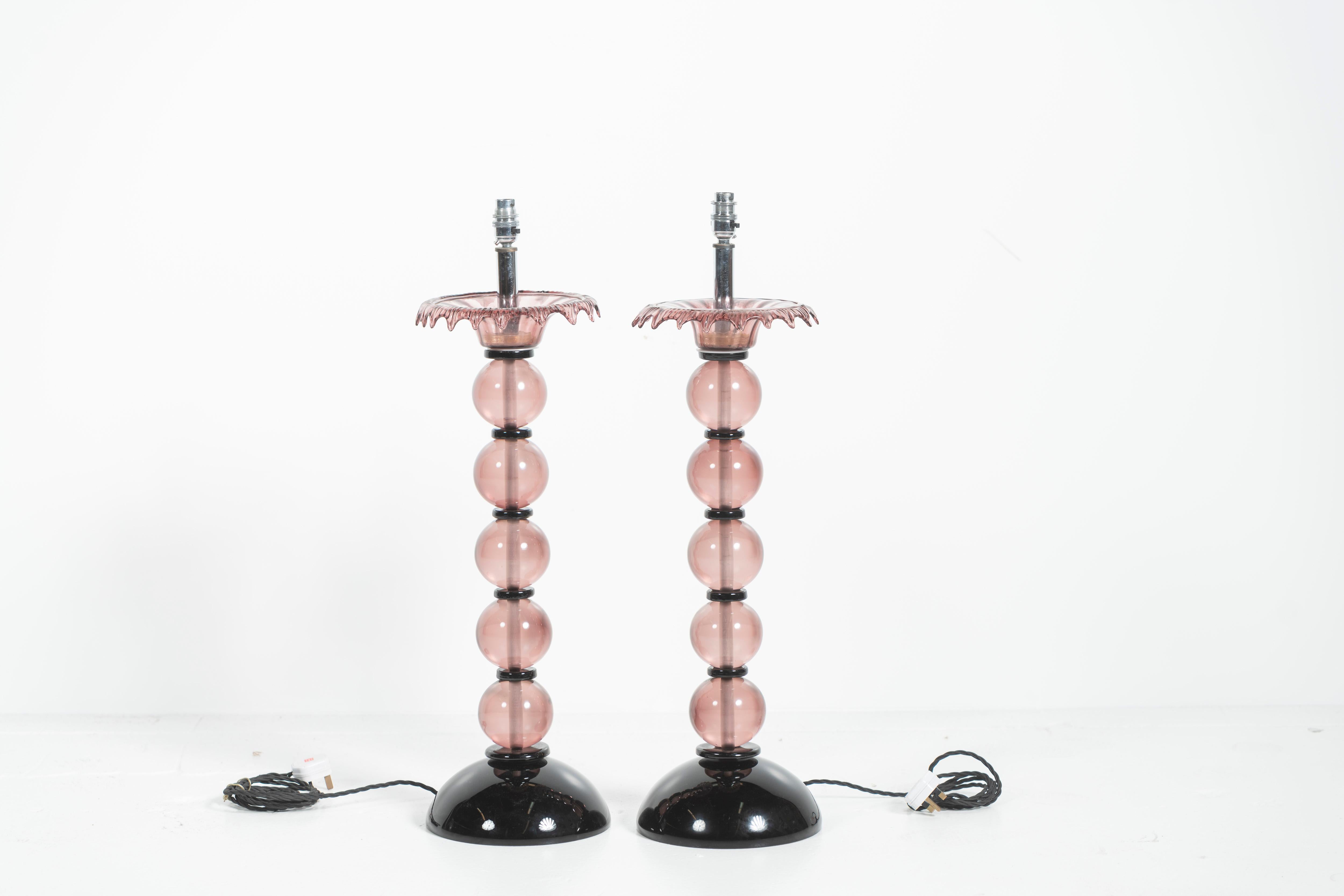 Whether in your bedroom or living room, these modern lamps,with pale pink and black glass, bring the timelessness of Mid-Century design to any space. Add the perfect shades and enjoy the beauty of colored glass lighting. Sold only as a pair.