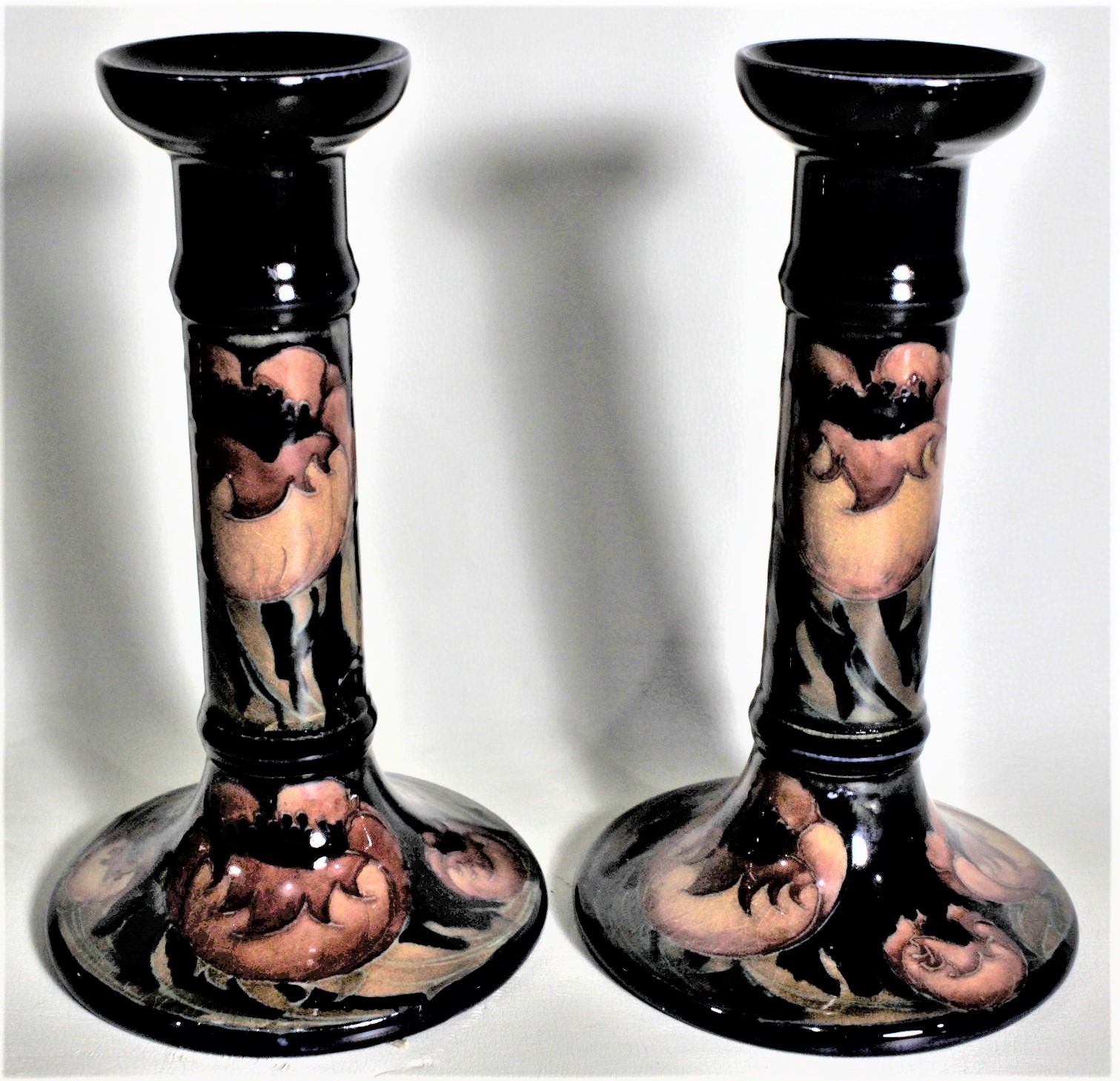 This pair of art pottery candlesticks or candle holders was done by the Moorcroft Pottery company of England in circa 1939 using their signature deep cobalt, appearing almost black in this case, blue ground and done in their 'Poppy' pattern. The