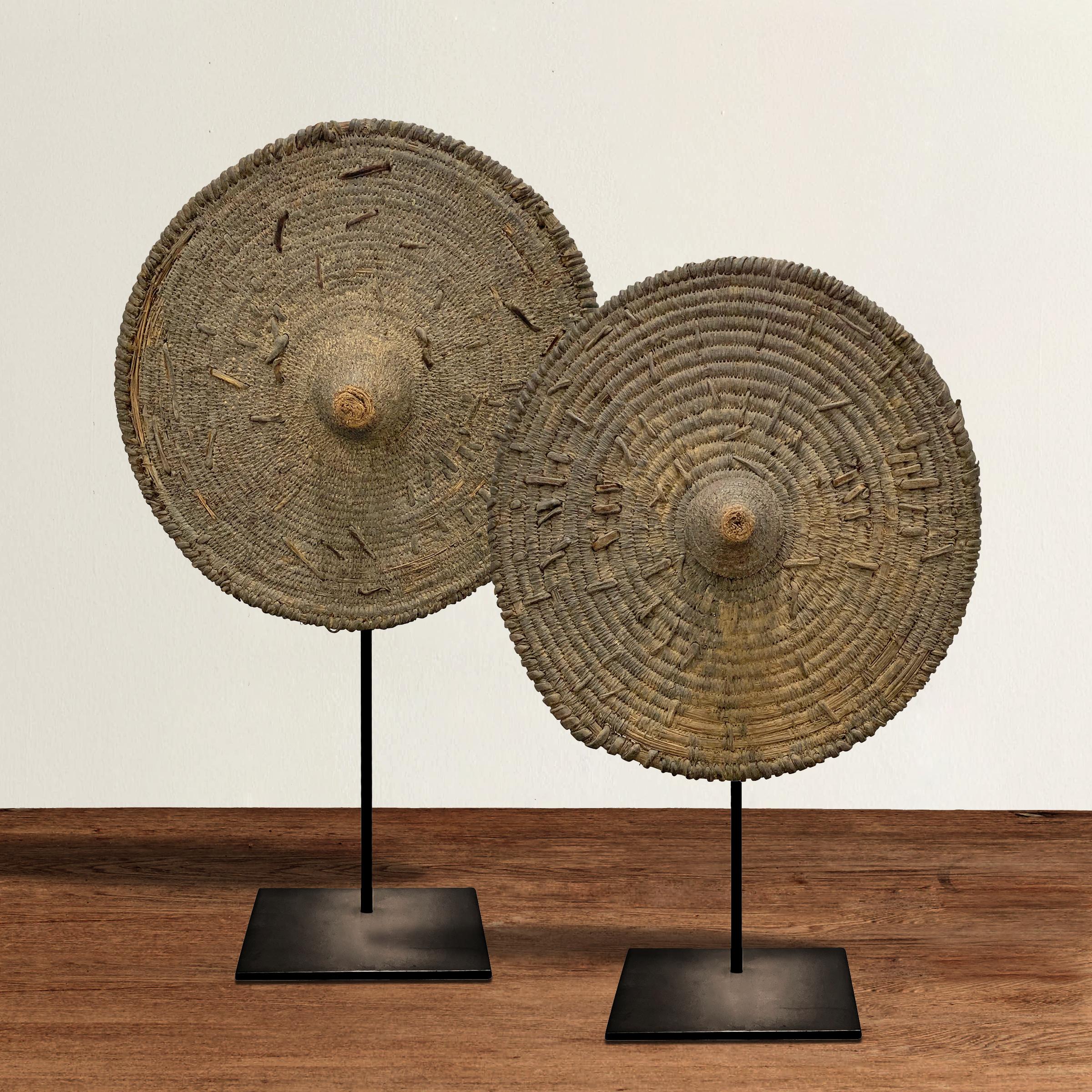A pair of wonderfully sculptural early 20th century handwoven wicker shields from the Tamberma people of Togo, mounted on custom steel stands.