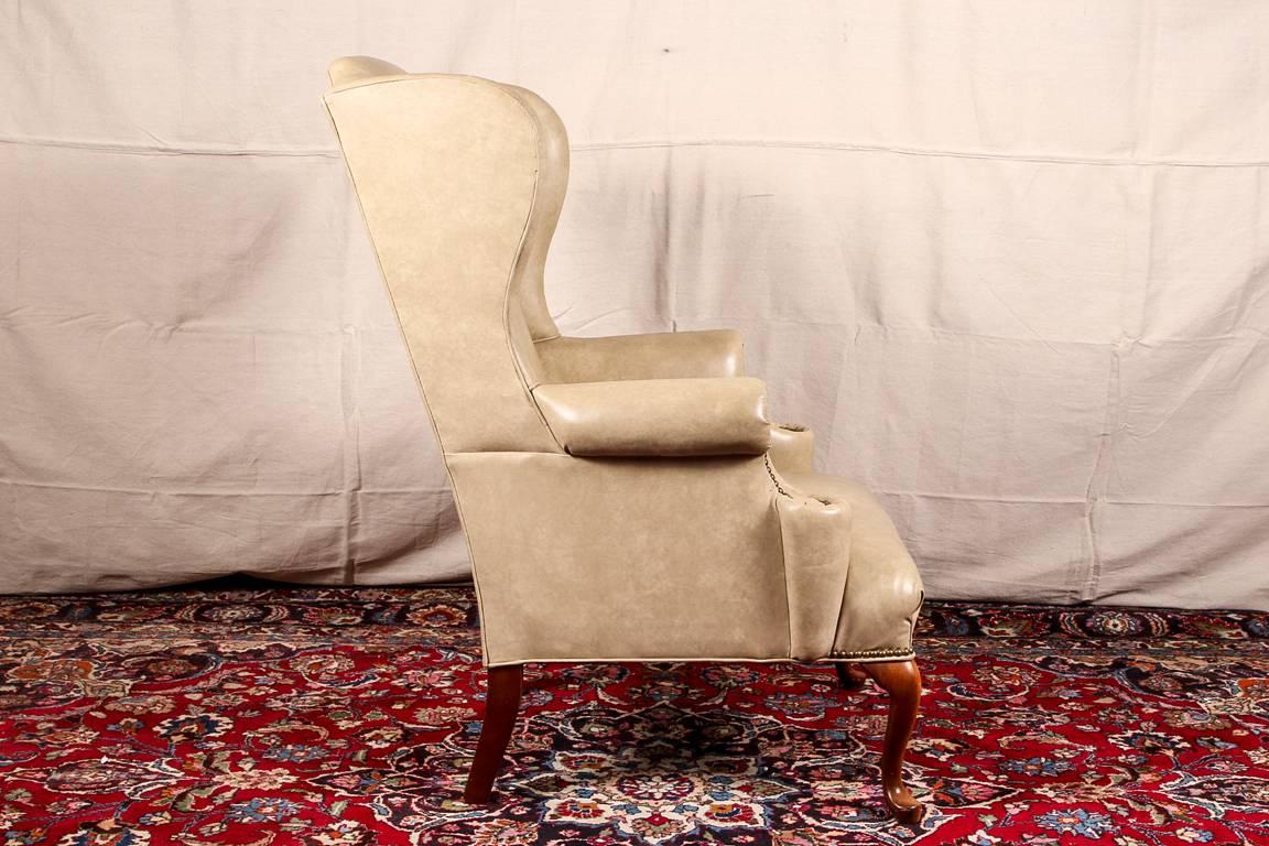 Pair of tan faux leather wing chairs, nail head trim on the front of the arms and along the fronts of the seats, raised on walnut cabriole legs in front and square splayed ones at back. 

Condition: Expected wear and signs of use including some