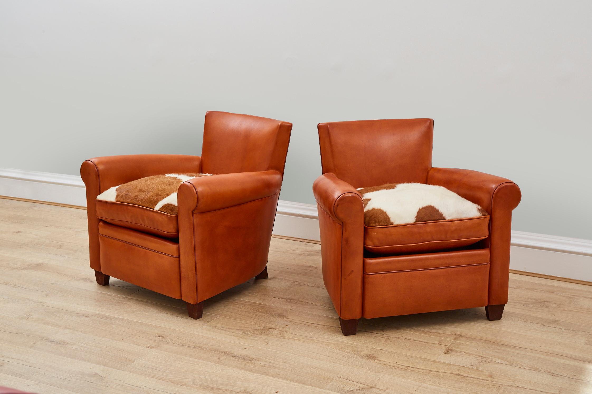 A stylish pair of tan leather armchairs featuring reversible seats -tan leather on one side with tan and white natural cow hide to the other. 

These chairs have been hand made with traditional methods - steel studded detail to the back of the