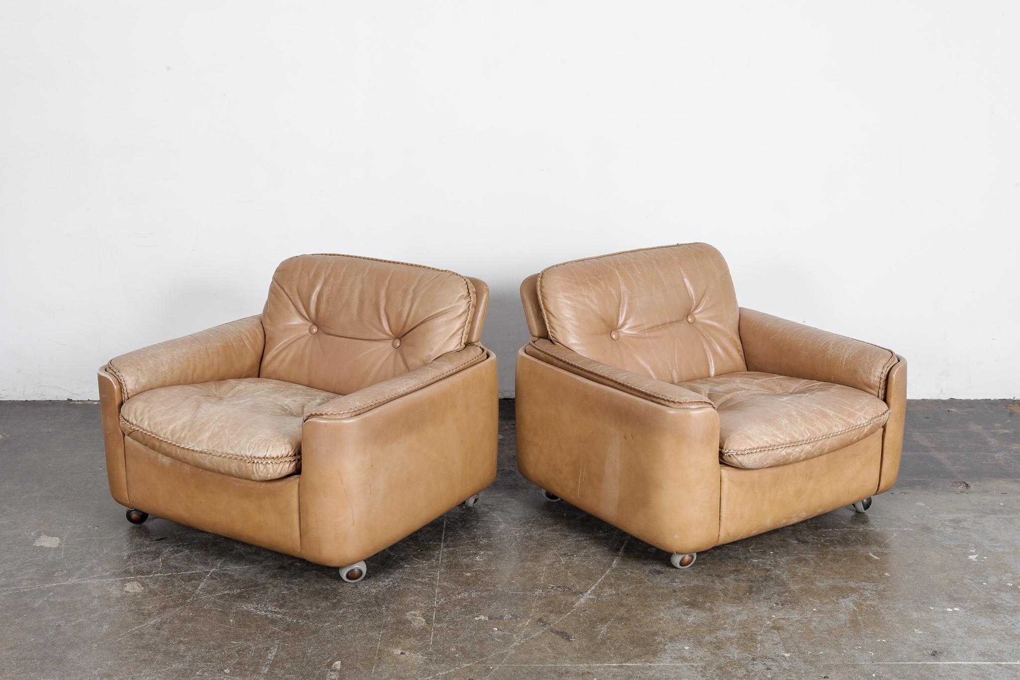 Pair of low lounge chairs in original tan leather with baseball seam stitching, sitting on 4 casters with button tufted backs and seats. Designed by Sigurd Ressell for Vatne Mobler, 1960s. Beautiful patina on both chairs by no tears or gouges.