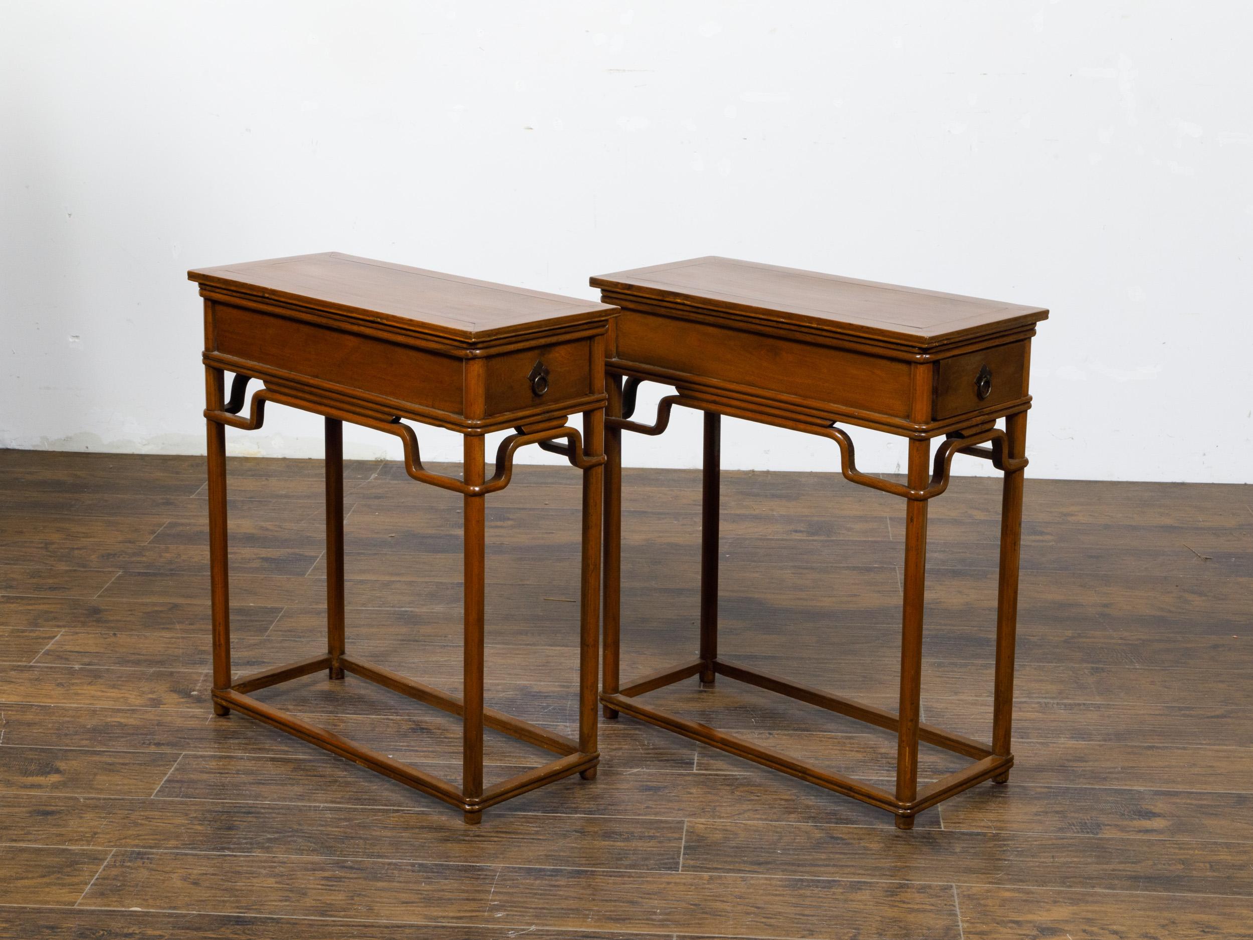 A pair of teak wood console tables from the 19th century with lateral drawer and humpback stretchers. This pair of 19th-century teak wood console tables emanates the timeless elegance and sturdy craftsmanship characteristic of the period. Each table