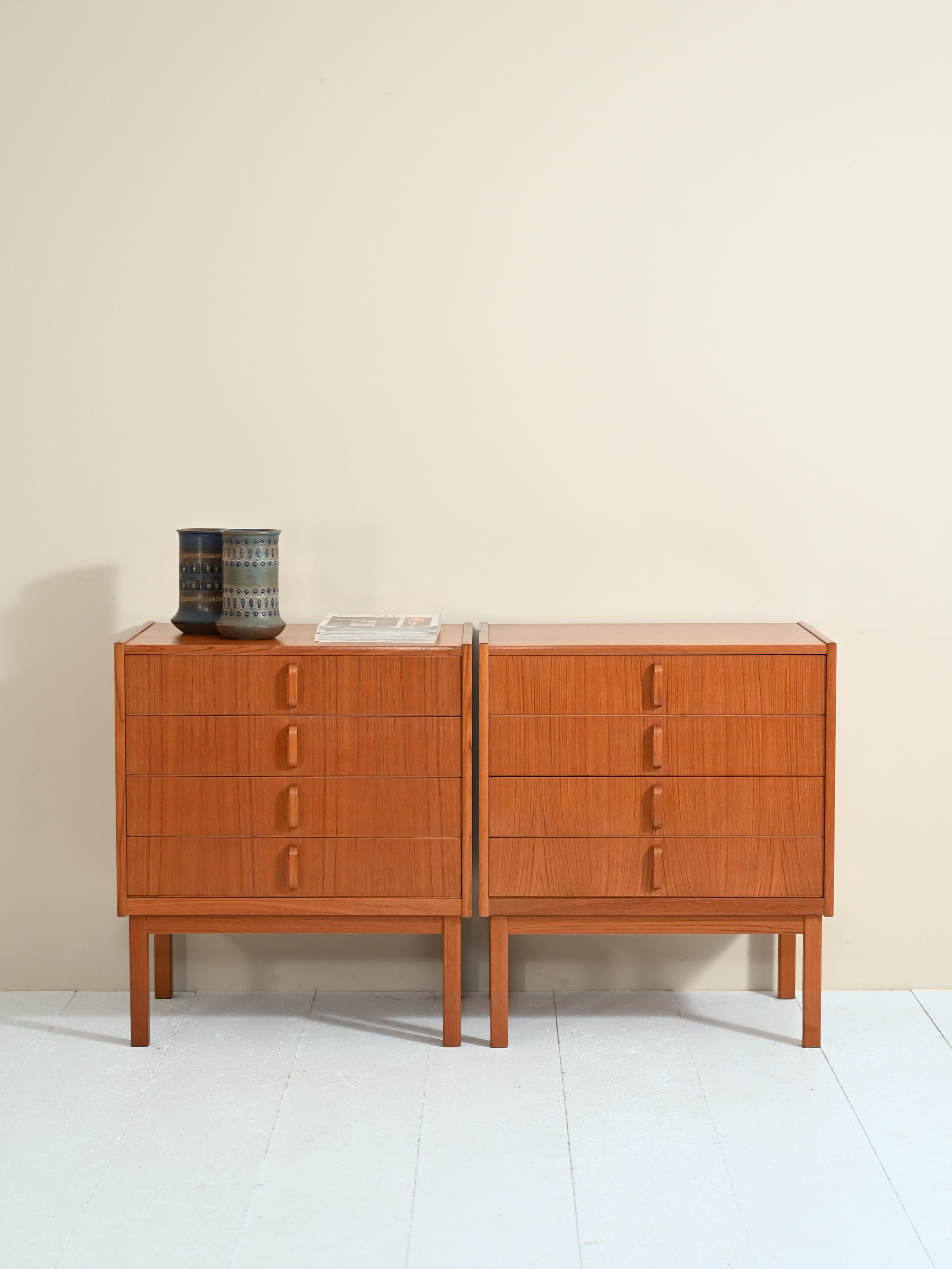 Pair of drawer chests with stamp of authenticity, originals from the 1960s.

Simple, square lines characterize these teak dressers, embellished by the protruding curved wood handle of the drawers.
The warm hue and pronounced teak wood grain make