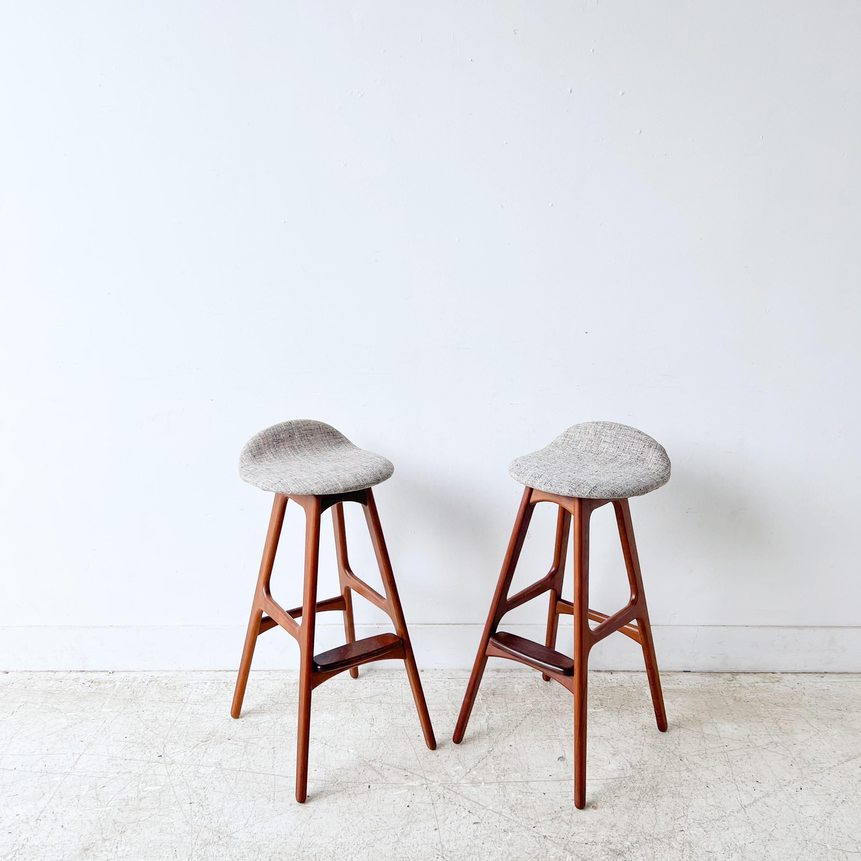 Pair of sleek bar height teak stools by Erik Buch for O.D. Møbler. Erik Buck is known for the Scandinavian and functional style of his pieces of furniture. Some light scuffing/scratching to the teak wooden frames from age/wear. New beige and grey