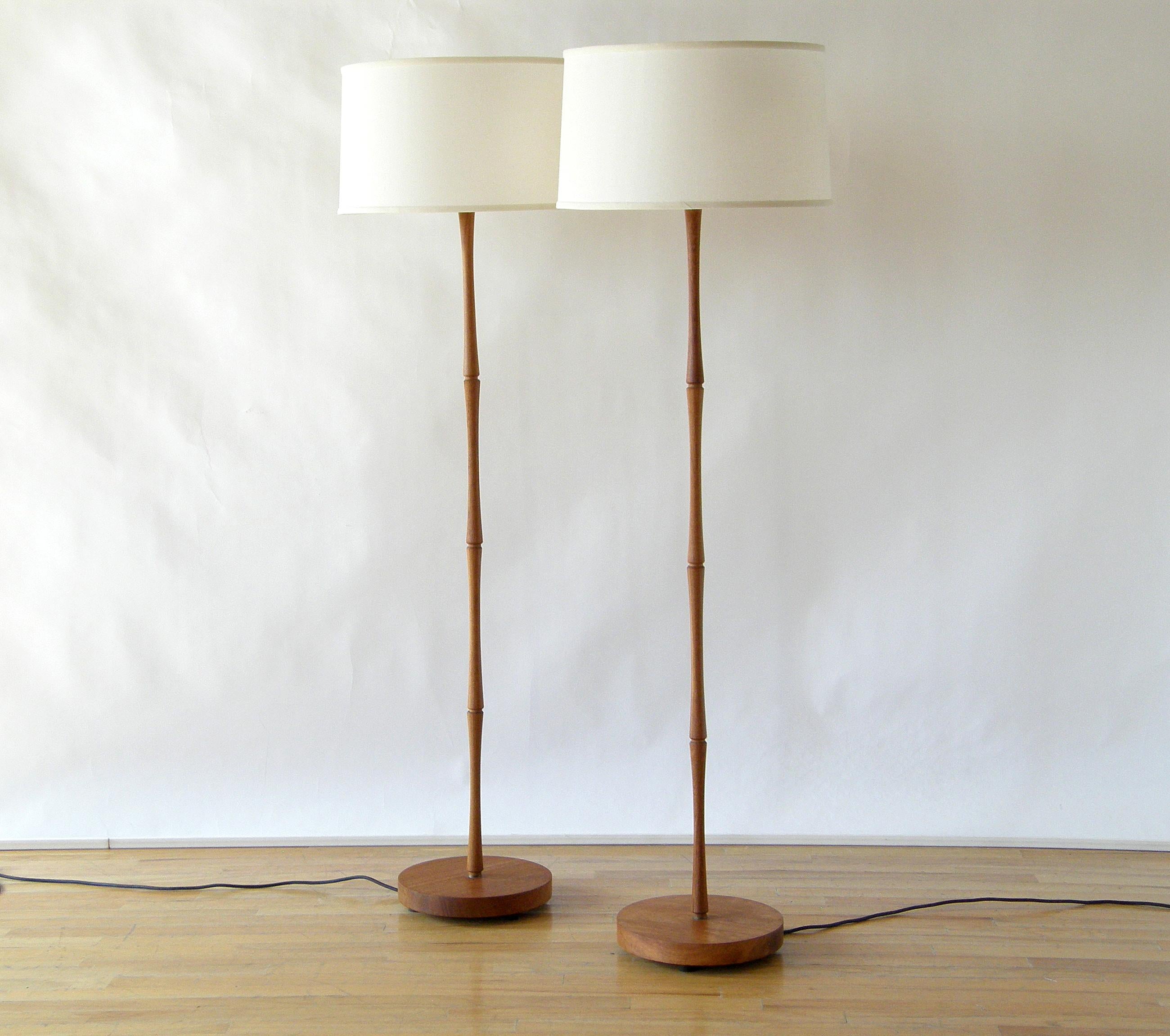 This pair of teak floor lamps have a stylized faux bamboo design to their stems. The segments are finely turned with an elegant hourglass shape representing the internodes of a bamboo stem. There are notched points between their flared ends,