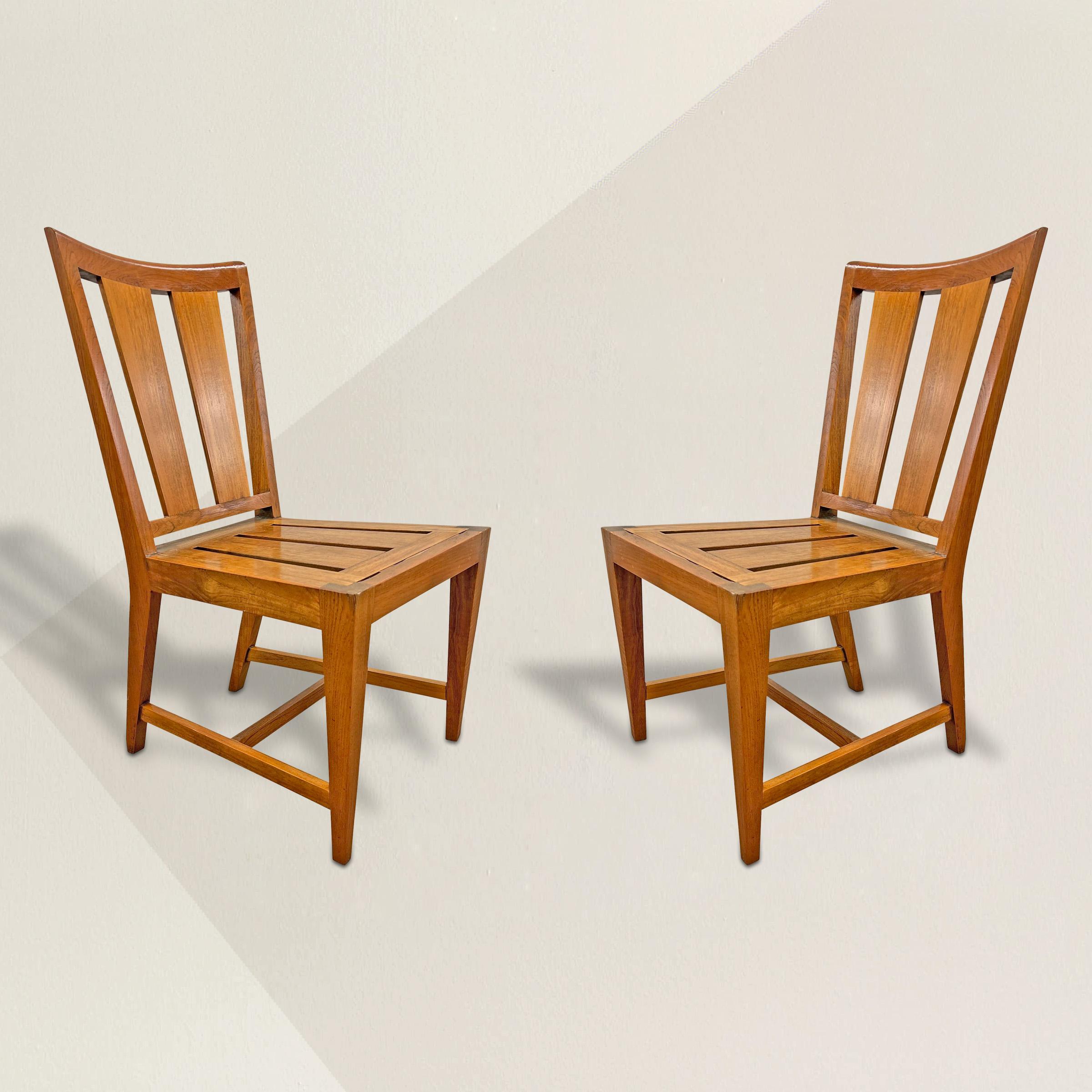 A strong and bold pair of 20th century American modernist teak wood side chairs, each with gently curved and sloping crestrails, splat backs and seats, and square tapered legs. Perfect at your breakfast table, flanking your entry console, or against