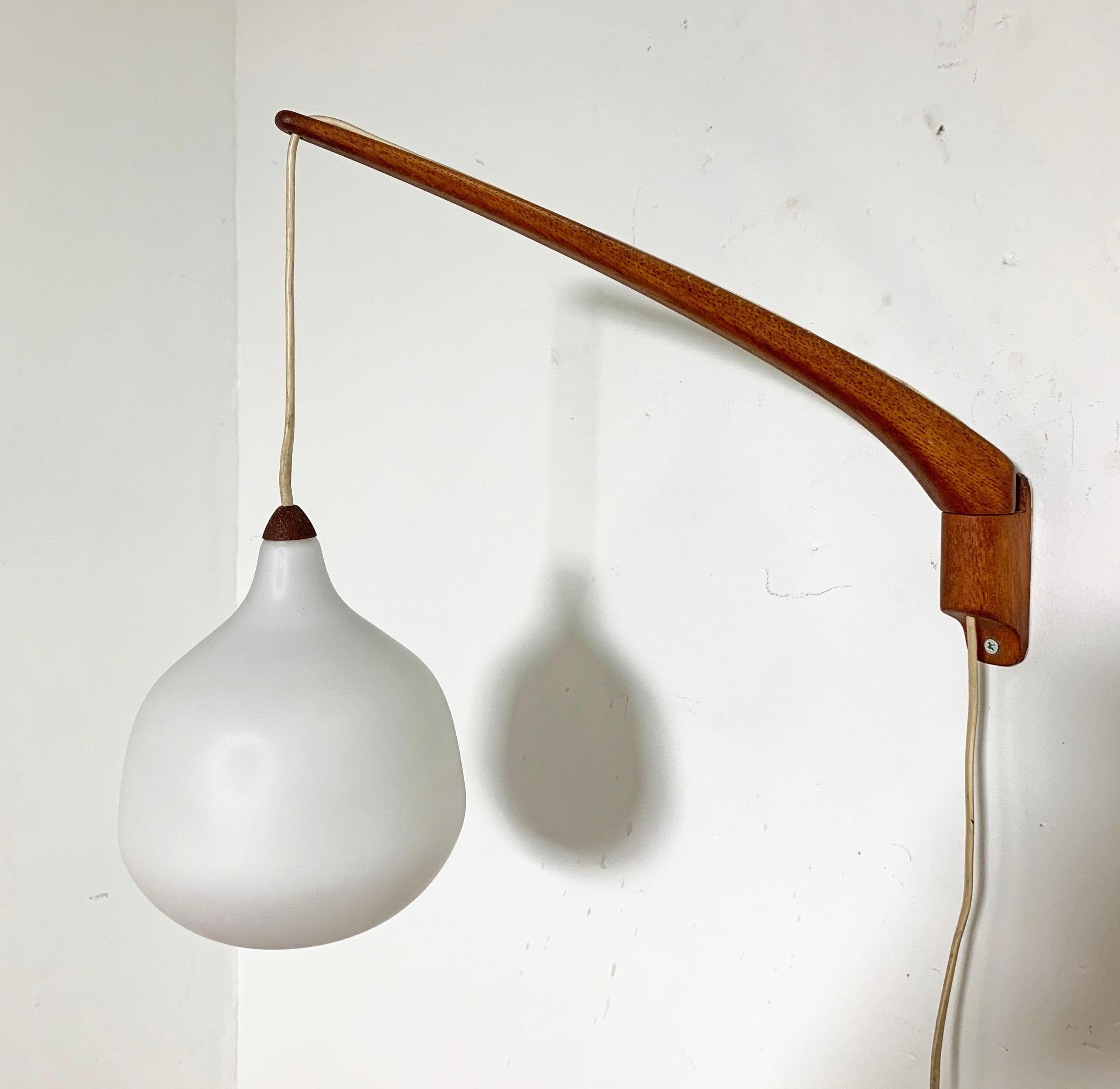 Pair of swing arm teak and opaline glass wall sconces designed by Uno & Östen Kristiansson for Luxus circa 1950s. 

 Pendant drop height and arm position in relation to the wall are adjustable. Maximum depth from wall is 17