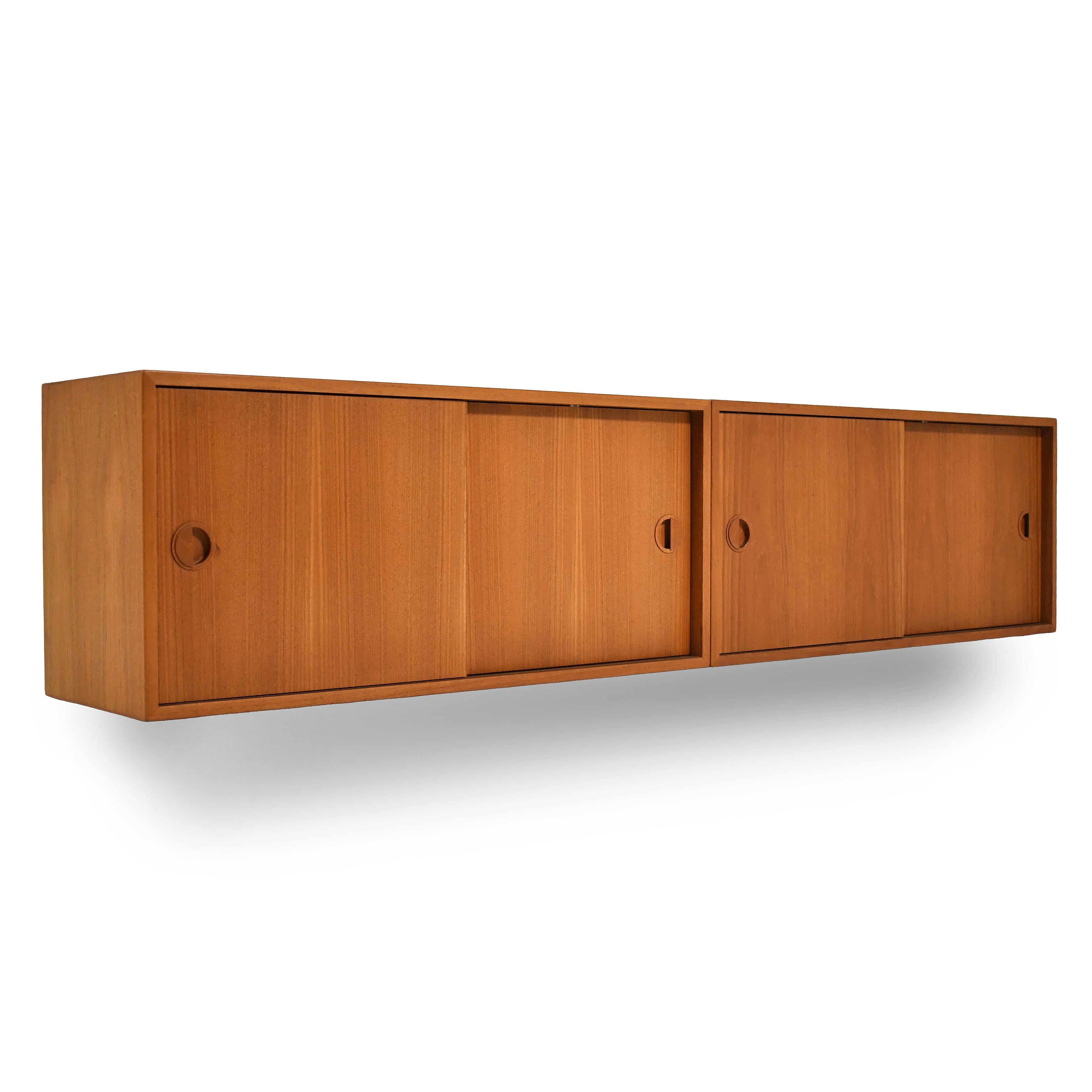 This handsome pair of teak floating wall cabinets were made in Denmark by Hansen and Guldbord (HG Furniture). The clean-lined cabinets have round sculptural pulls on the sliding doors which conceal adjustable shelves.

 These cabinets were used by