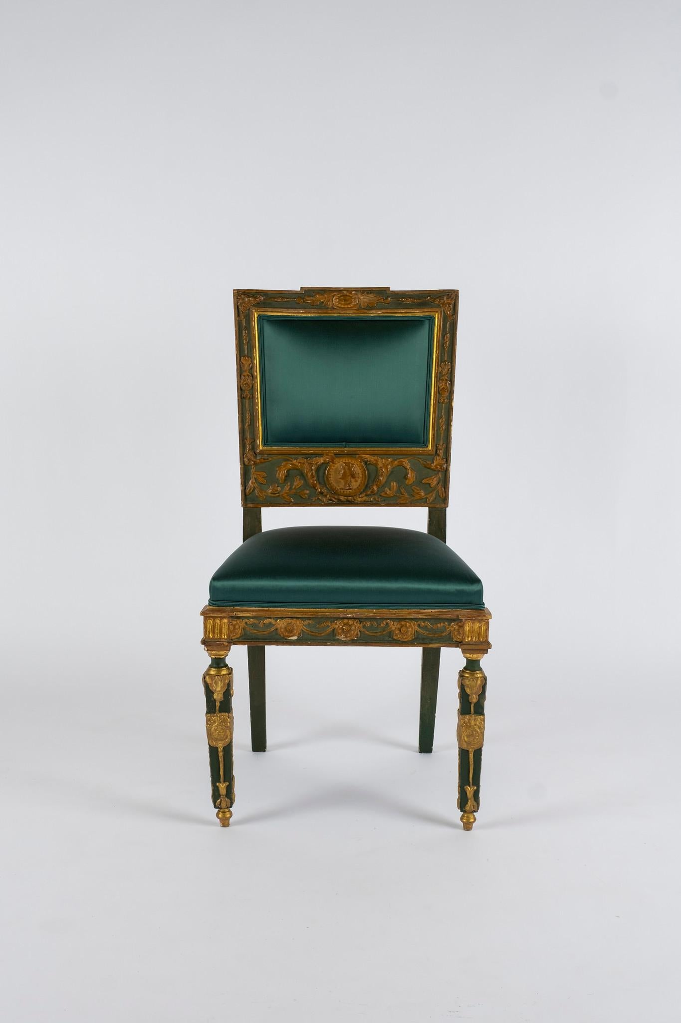 Pair of early 19th century French Empire painted and gilded side chairs newly upholstered in a luxurious teal heavy silk satin. These chairs feature detailed gilt ornamentation of head bust, swags and medallions.