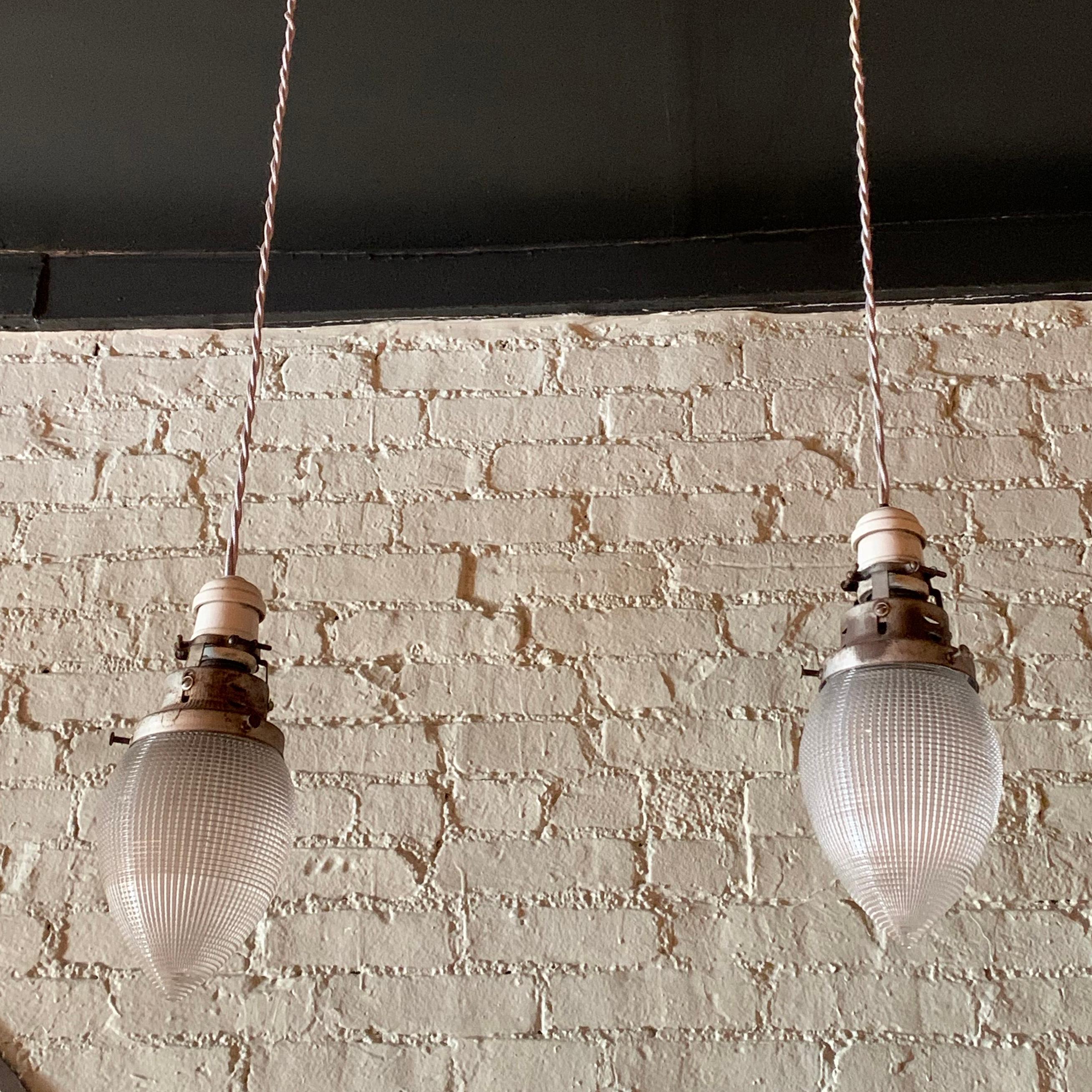 Pair of industrial pendant lights feature teardrop shape, prismatic, Holophane glass shades with porcelain and brass switch fitters newly wired with 36 inches of braided gray cloth cord.