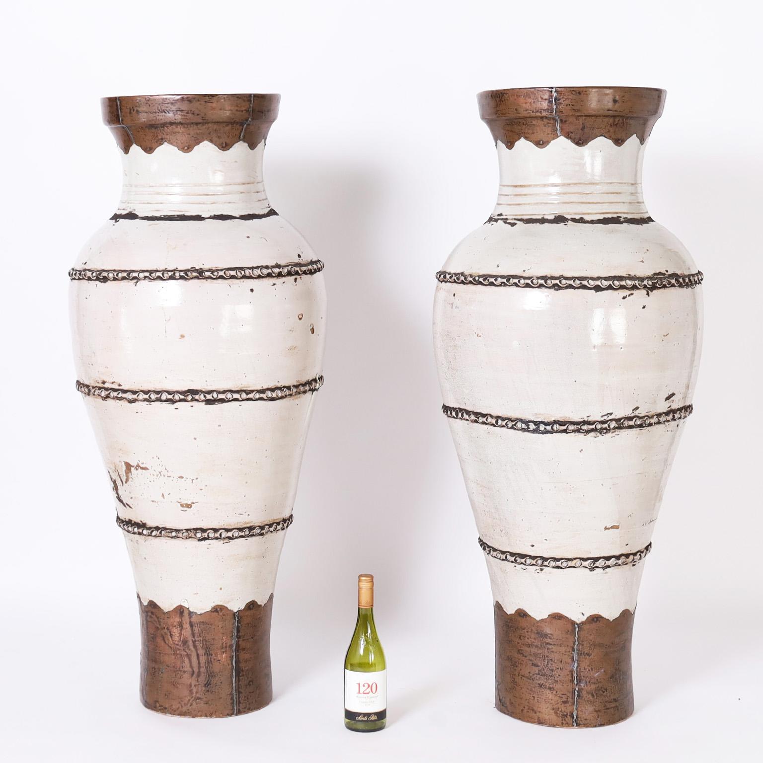 Intriguing pair of floor vases crafted in hand turned terra cotta in a grand scale with a white glaze and mounted with hammered copper lips and feet.