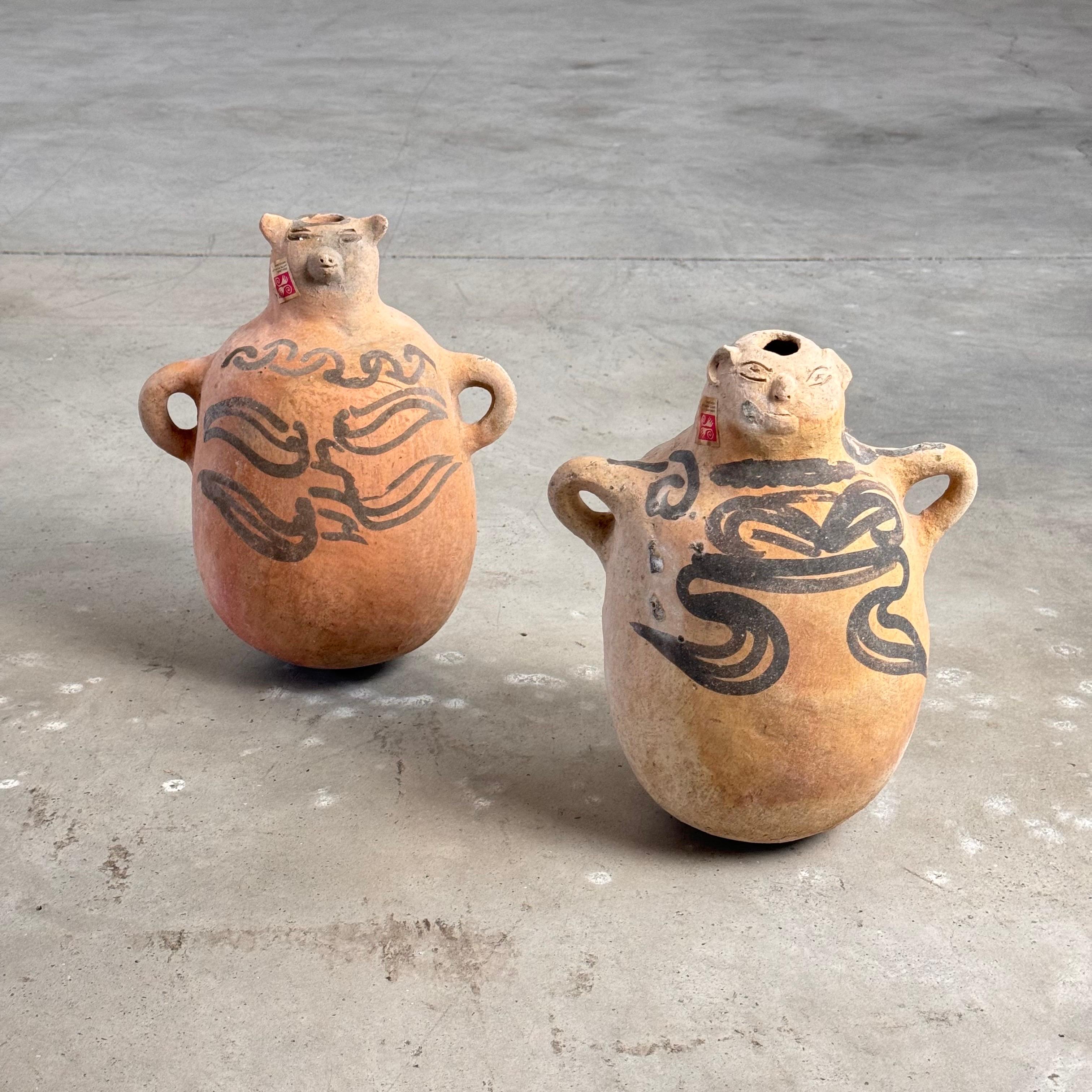 Questa eccezionale coppia di brocche da pulque in terracotta dipinte a mano, provenienti da Tuliman, Guerrero, negli anni '70, rappresenta un esempio distintivo di arte popolare messicana. Tradizionalmente utilizzate per trasportare il pulque, una