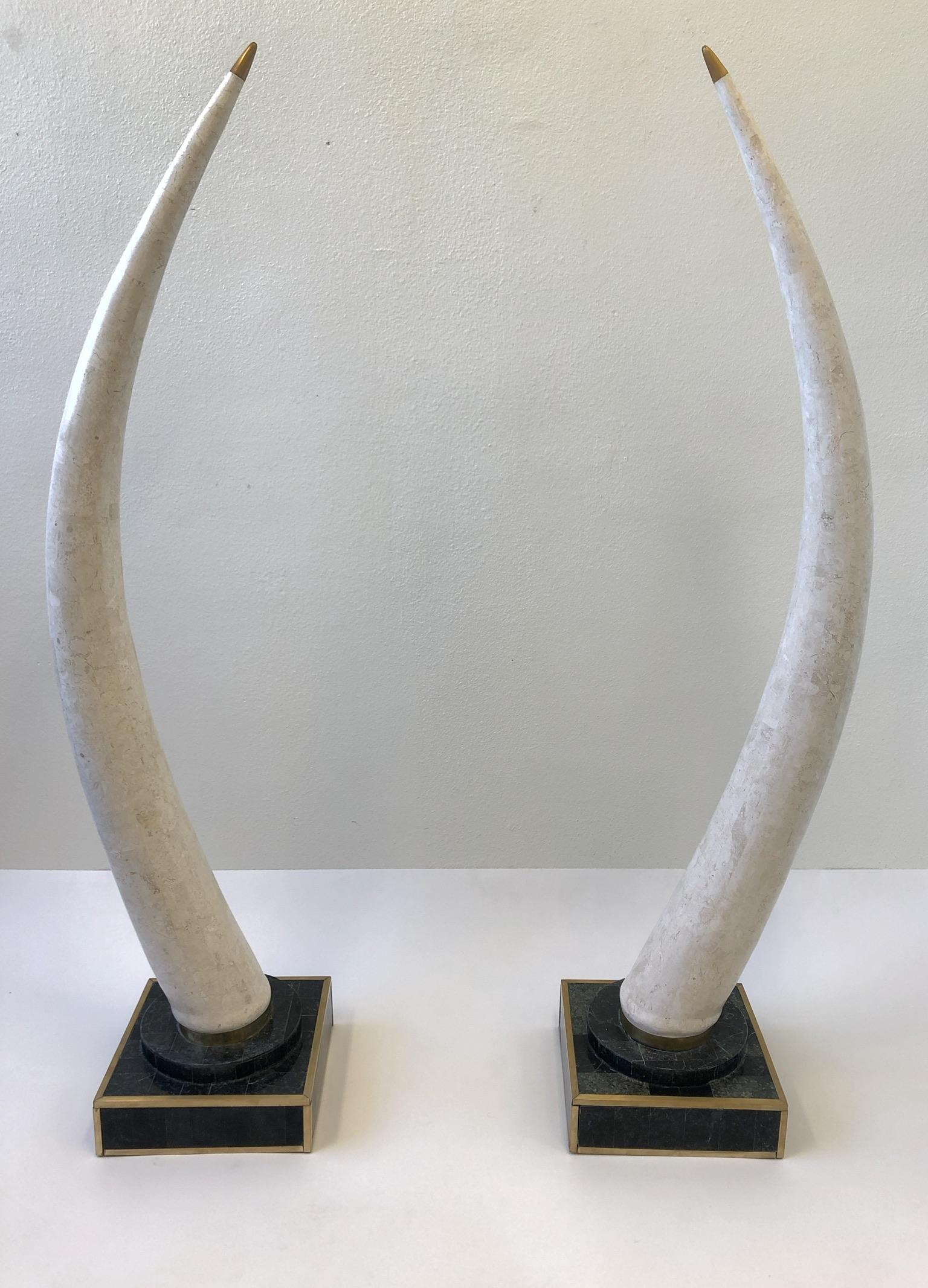 A pair of 1980s faux tusk by Marquis Collection of Beverly Hills. The tusk are constructed tessellated travertine and black marble with brass detail. This were placed outdoors on a covered patio so they show some age. The base is 14” by
