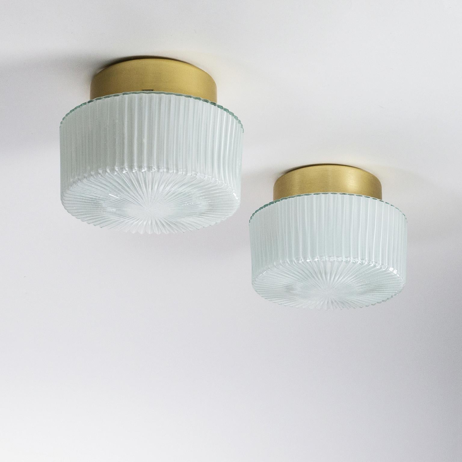 Pair of 1960s flush mounts or wall lights with textured glass diffusers on gold anodized aluminum backplates. The glass diffusers with radial grooves are lightly cased on the inside for a softer light dispersion. One original ceramic E27 socket with