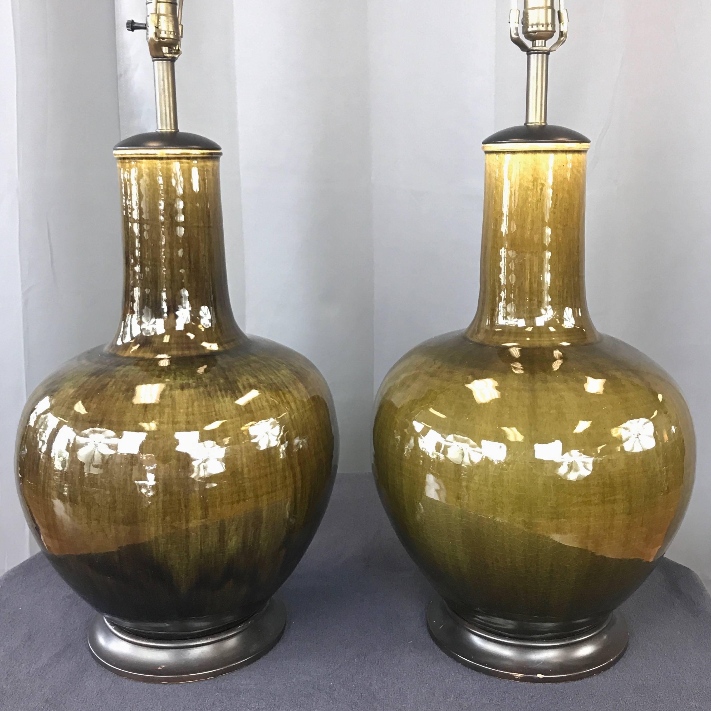 A very impressive pair of midcentury monumental green glazed ceramic table lamps by Thai Celadon Company.

Classic Asian form with ginger jar-shaped body and tall, robust neck. Finished in Thai Celadon Company’s signature dark olive “Jungle Jade”