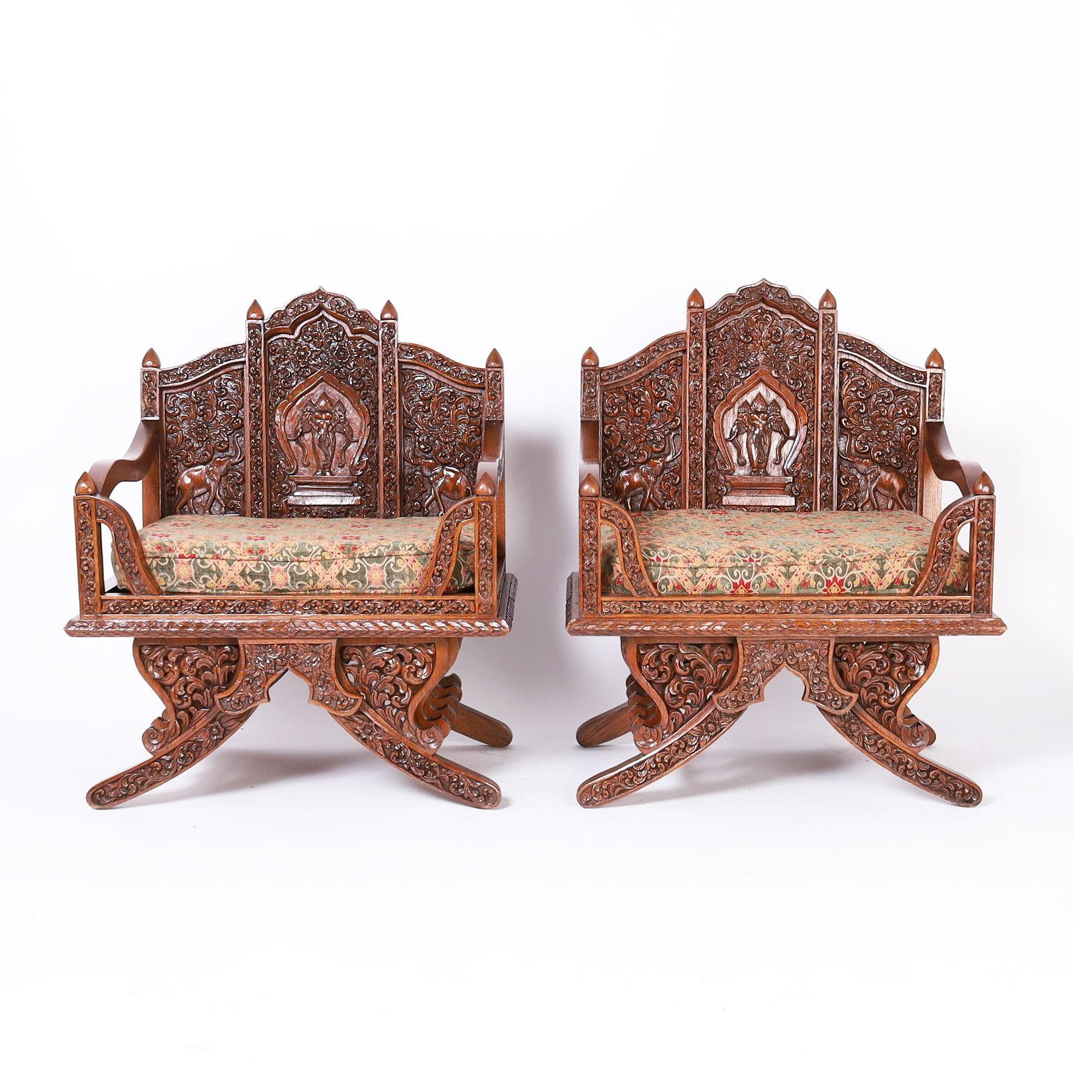 Paire de chaises de style selle d'éléphant fabriquées en bois de rose dans une forme thaïlandaise caractéristique, sculptées à la main représentant des éléphants, qui sont un symbole de fortune, dans un champ floral élaboré, et avec des sculptures