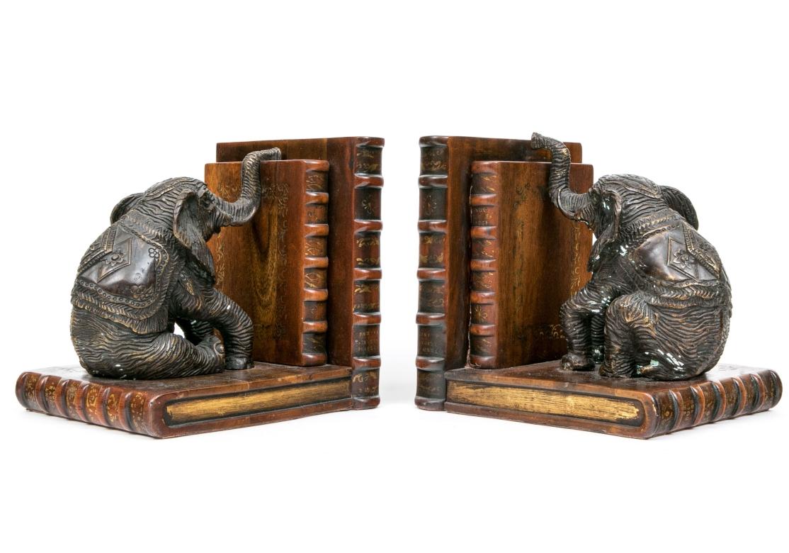 Grande e imponente set di fermalibri Theodore Alexander che raffigura elefanti in metallo patinato seduti in cima a un basamento in legno a forma di libro. Gli elefanti si trovano di fronte a due libri finti con abbellimenti dorati. Il fondo è