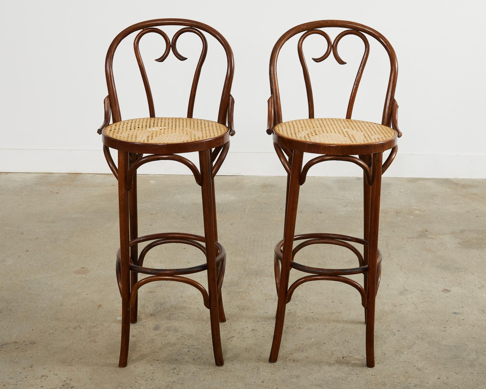 Rare pair of mid-century modern bar stools crafted from bentwood after Thonet. The stools feature a classic heart motif back crafted from gracefully curved beech. The round seat has woven cane inset and is supported by long straight legs conjoined