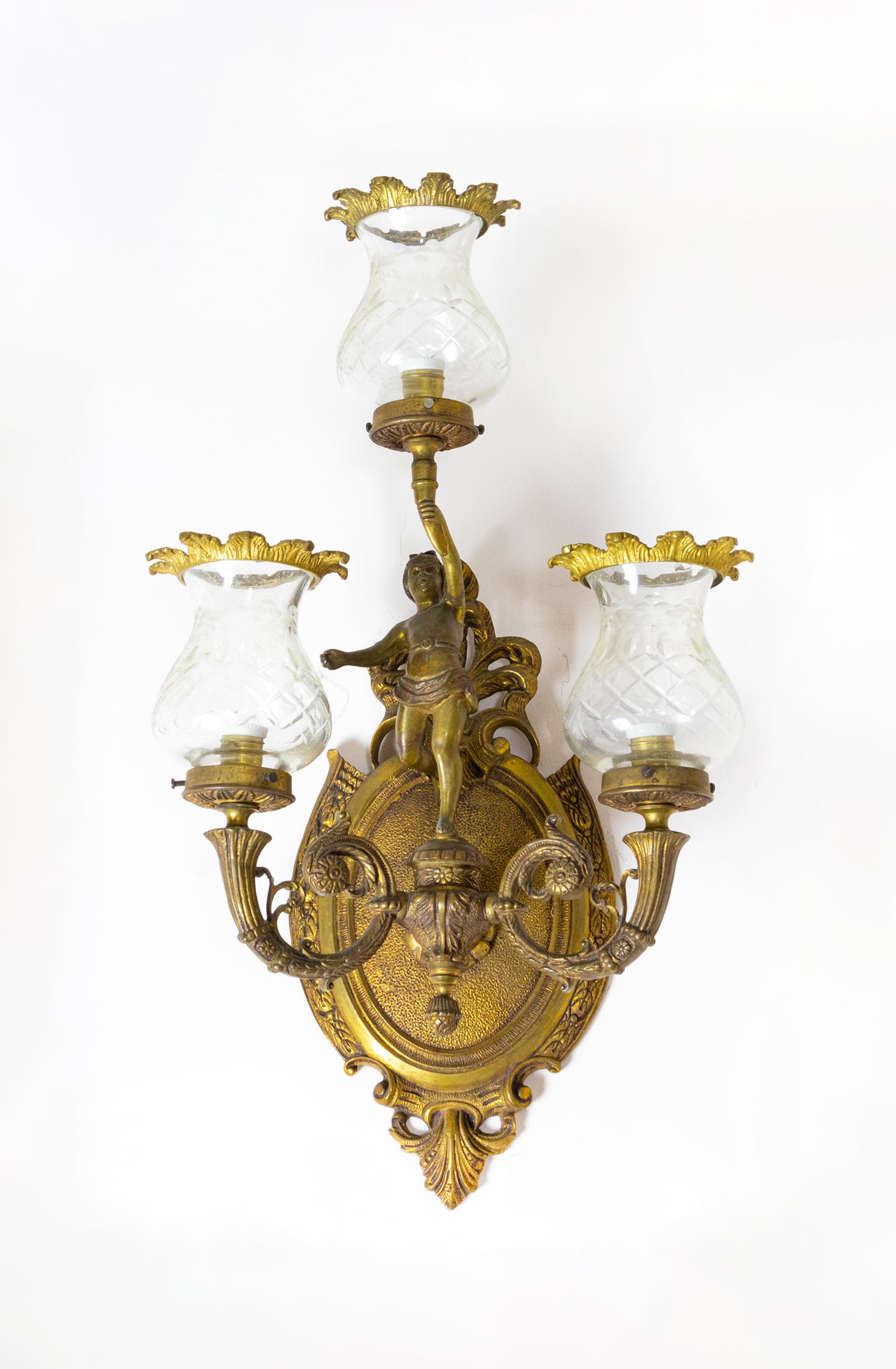 Portuguese crafted during the early 20th century, this remarkable pair of bronze and brass sconces showcases an extraordinary figurative design with three arms. 

Adorned with a captivating sculpture at the base, these sconces also feature three