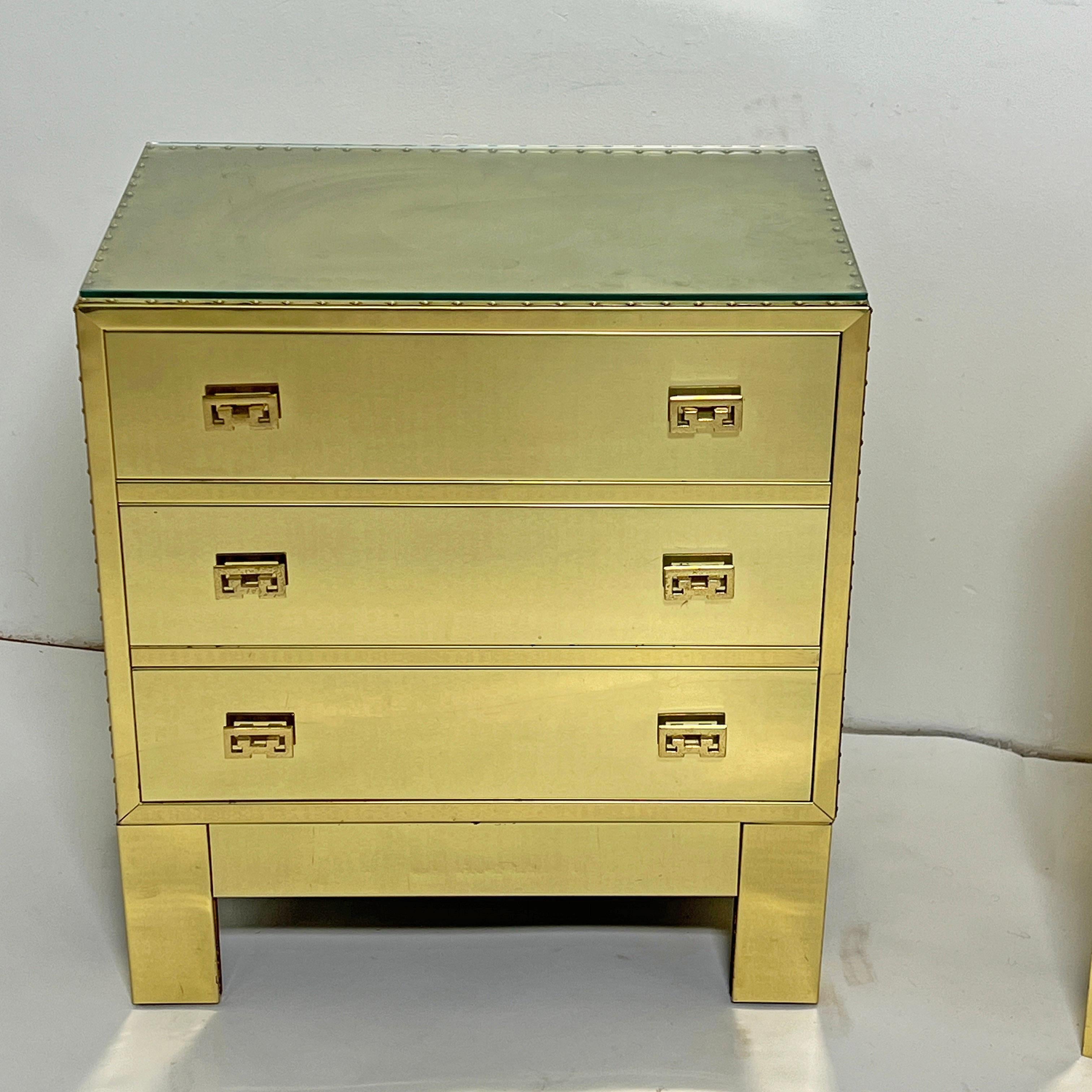 A pair of nightstand height three drawer brass clad chests with stud details, most likely by Sarreid Ltd., circa 1970s. Includes a pair of glass tops, though could be used without (see final two images).