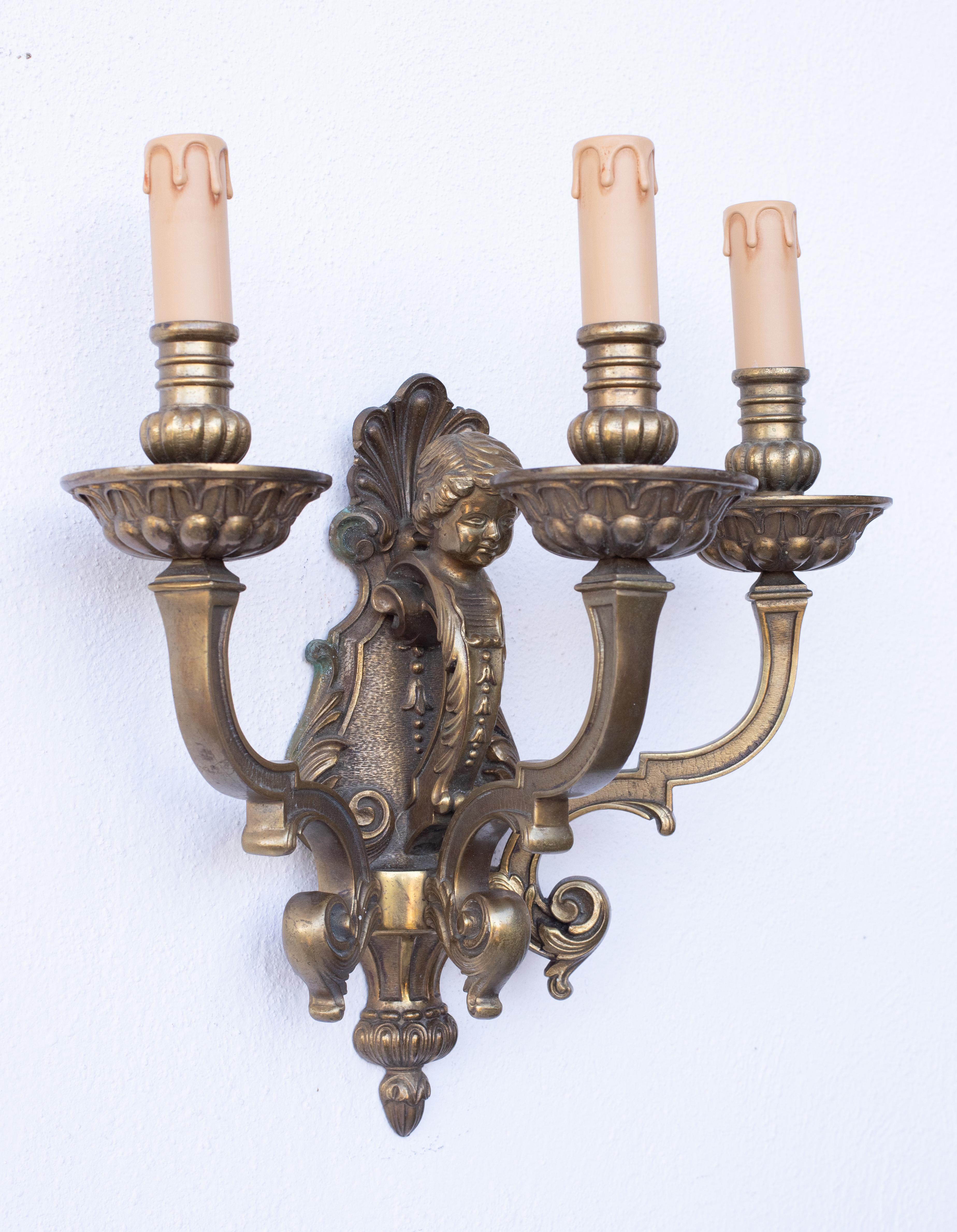 A massive pair of three-light brass wall sconces in the Louis XVI style, decorated with two little boys with phytomorphic motifs on their heads.

Height 40 centimeters, 32 without candelabra.
Width 35 centimeters.
Depth 20 centimeters.