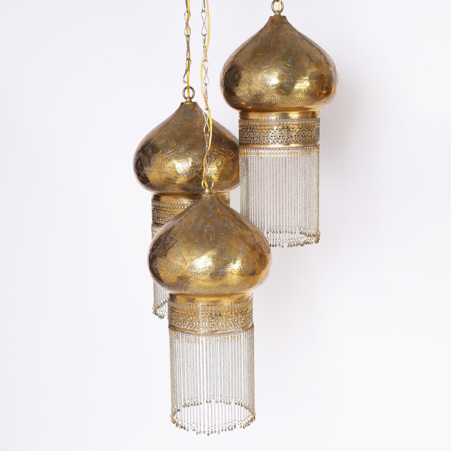 Pair of exotic Moroccan light fixtures each with three onion dome form pendants crafted in brass, tooled, inscribed, perforated, and finished with brass tassels in the Orientalist manner. Hand polished and lacquered for easy care.