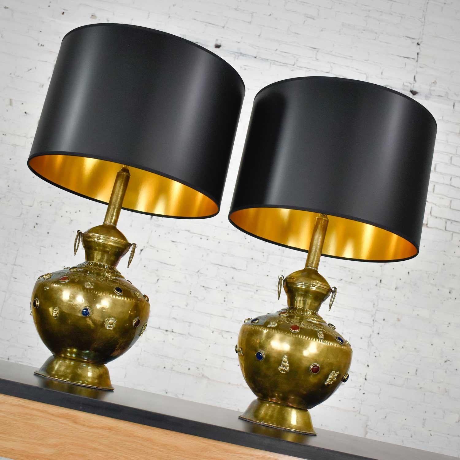 Stunning pair of hand hammered Tibetan brass lamps with glass jewels, etched and applied details, and new black Fenchel drum shades. Beautiful condition with wear as you would expect with vintage pieces. Very handmade, new wiring, and sockets with