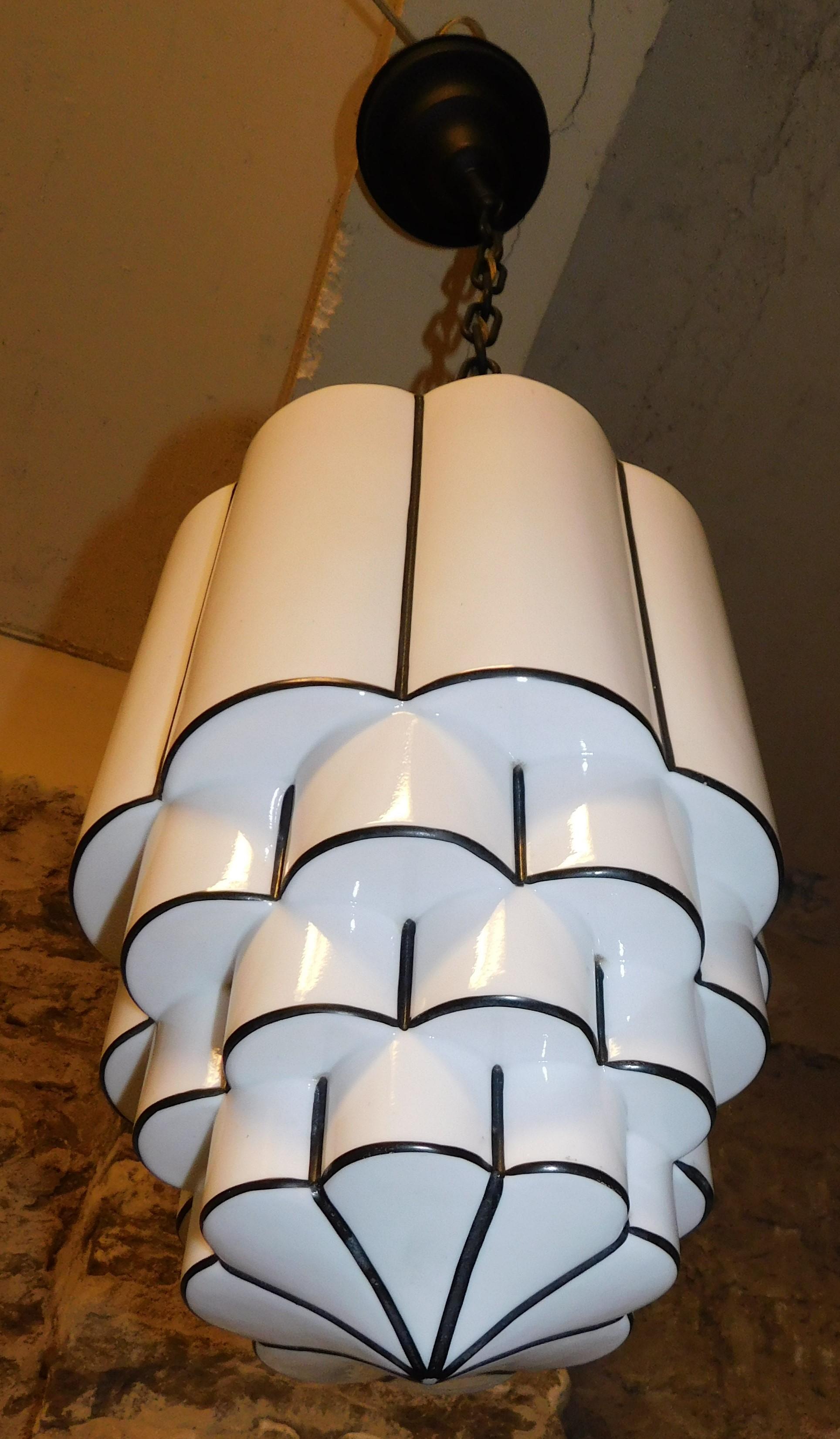 Beautiful pair of Art Deco pendant lights featuring tiered skyscraper milk glass with a dark blue trim, circa 1930. The shades measure 15 inches high and 10 inches round at their biggest point and 38 inches from the top hanging chain to the bottom