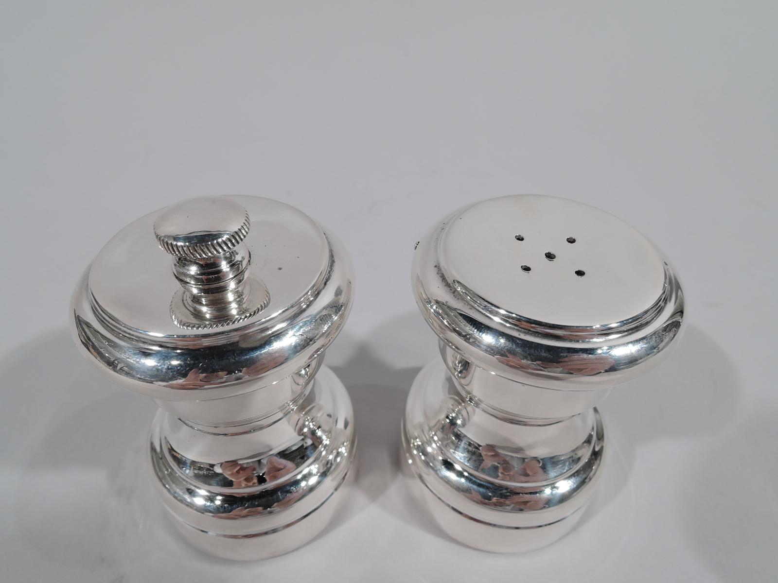 Pair of Modern sterling silver salt shaker and pepper mill. Retailed by Tiffany & Co. in New York. Each: Spool form with flat bellied top. Salt top pierced. Pepper top rotates with threaded finial. Both pieces fully marked including retailer’s