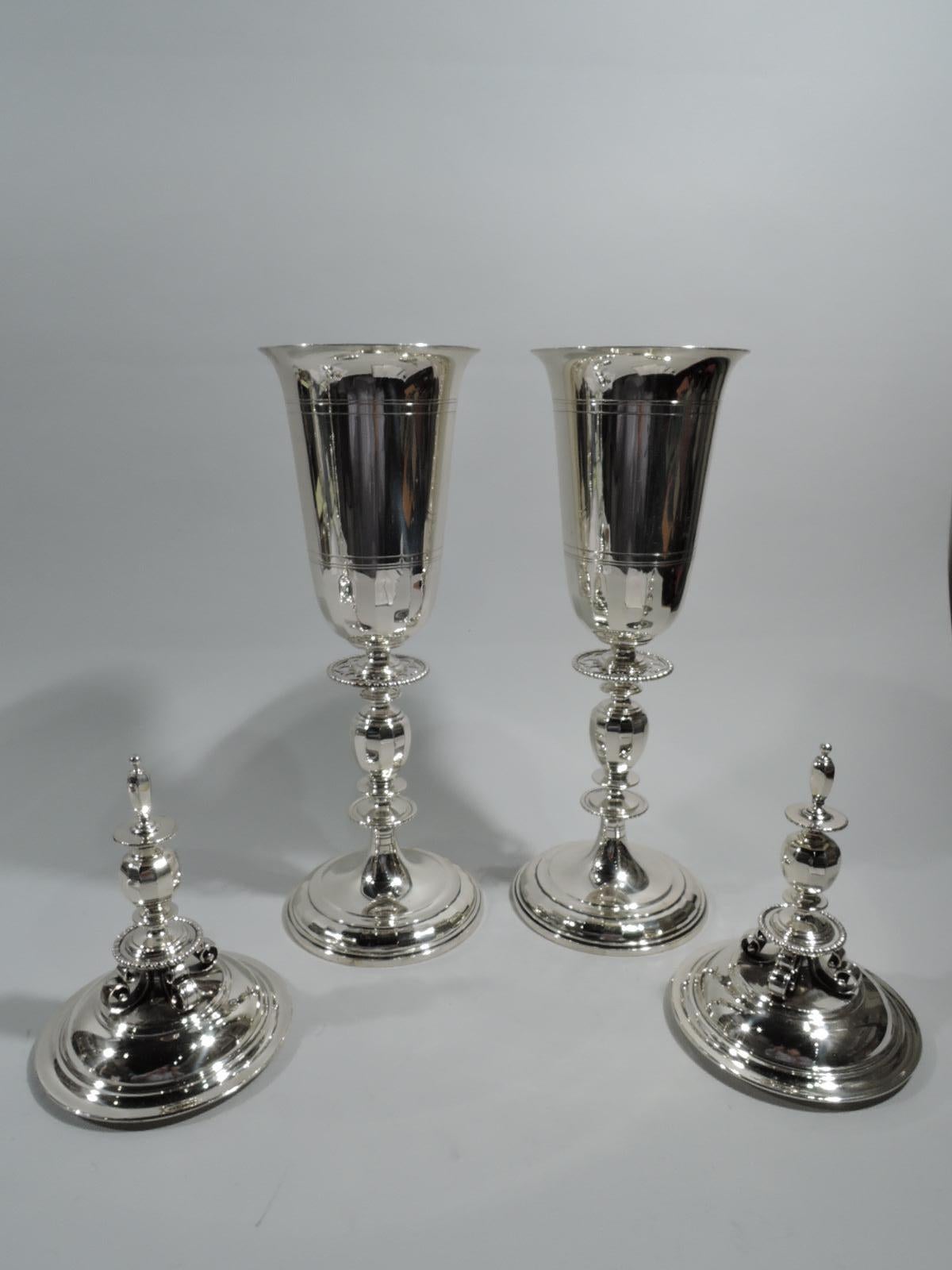 Pair of Art Deco classical sterling silver covered urns. Made by Tiffany & Co. in New York, ca 1919. Each: Ovoid urn with tooled line borders. Cover domed with fancy finial comprising spool support with 4 scrolled brackets to which is mounted knops,