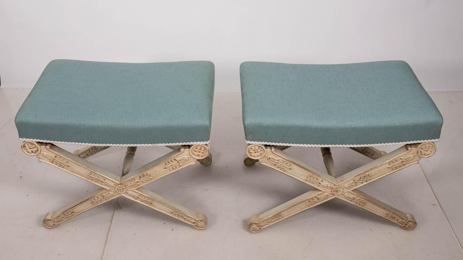 Contemporary pair of Louis XV style benches upholstered in Tiffany blue fabric and white trim. The pieces also feature white painted X-frame bases carved with bell flower motifs. Please note of wear consistent with age including distressed finish