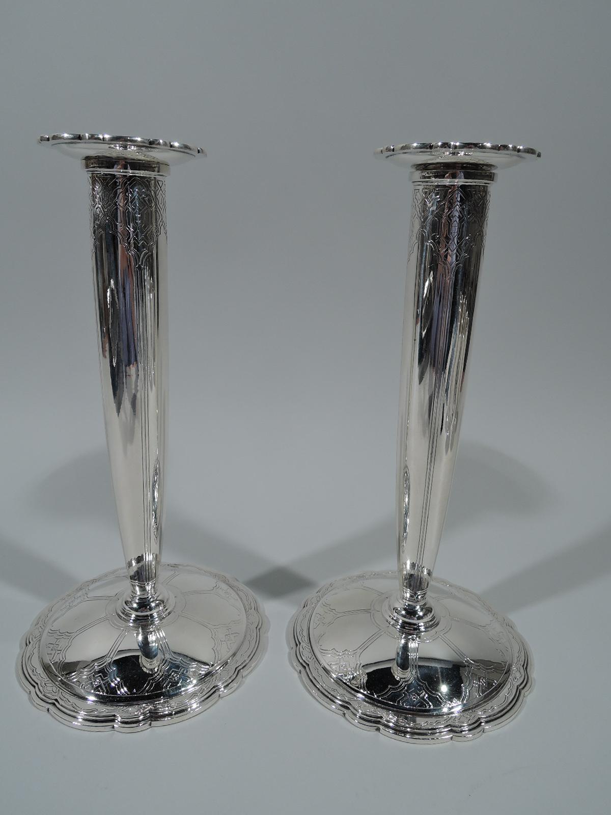 Pair of Art Deco sterling silver candlesticks. Made by Tiffany & Co. in New York. Each: Tapering shaft inset with detachable bobeche. Foot round and raised. Bobeche and foot rims have alternating small and wide scallops. Acid-etched ornament and