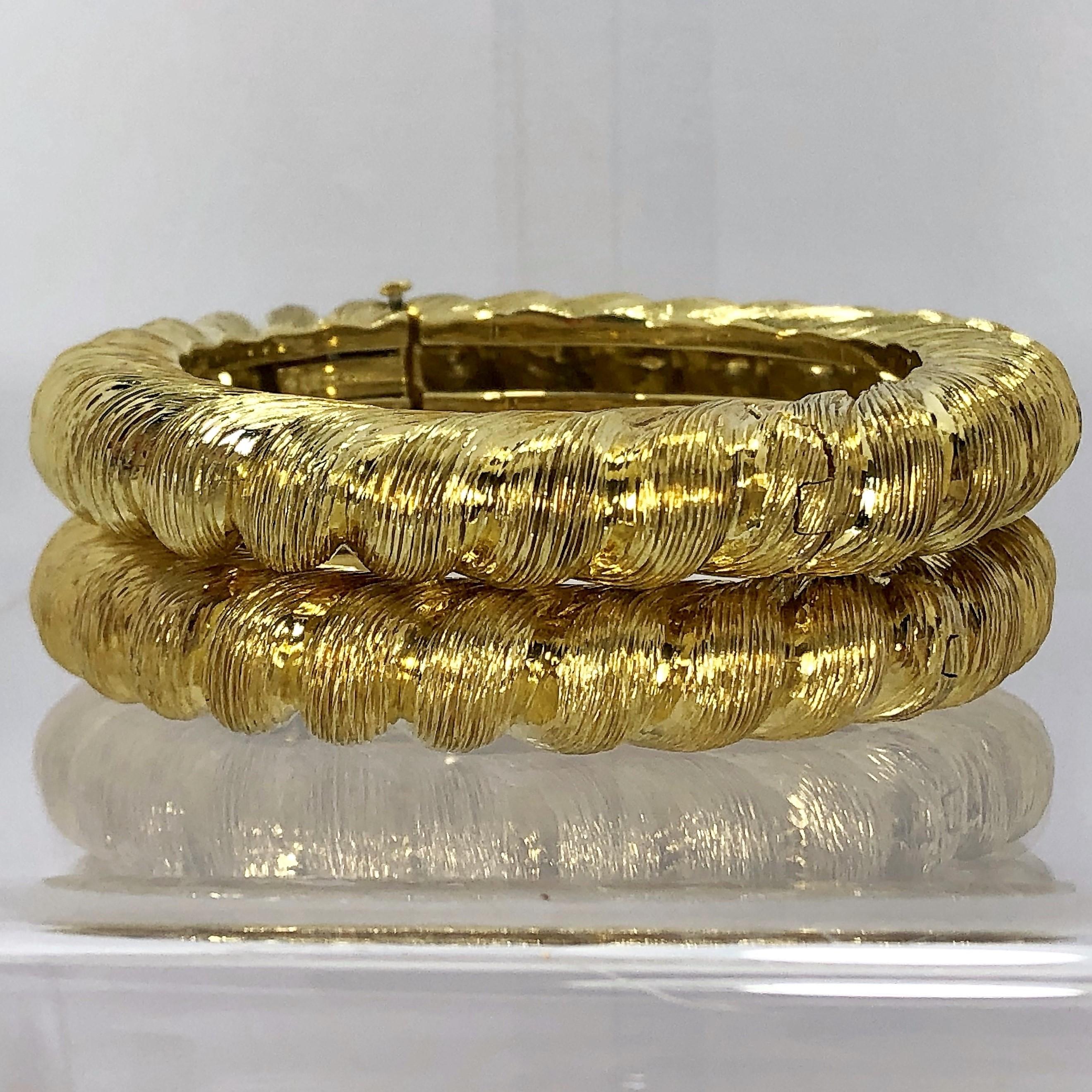 A matched pair of 18K yellow gold, 
bangle bracelets by Tiffany &Co.,
featuring a twisted rope design.
Can be worn individually or stacked 
as shown. Hinged on one side. Signed Tiffany and Co. 18k. Fits a small wrist 
size. Measuring 7/8 inch wide