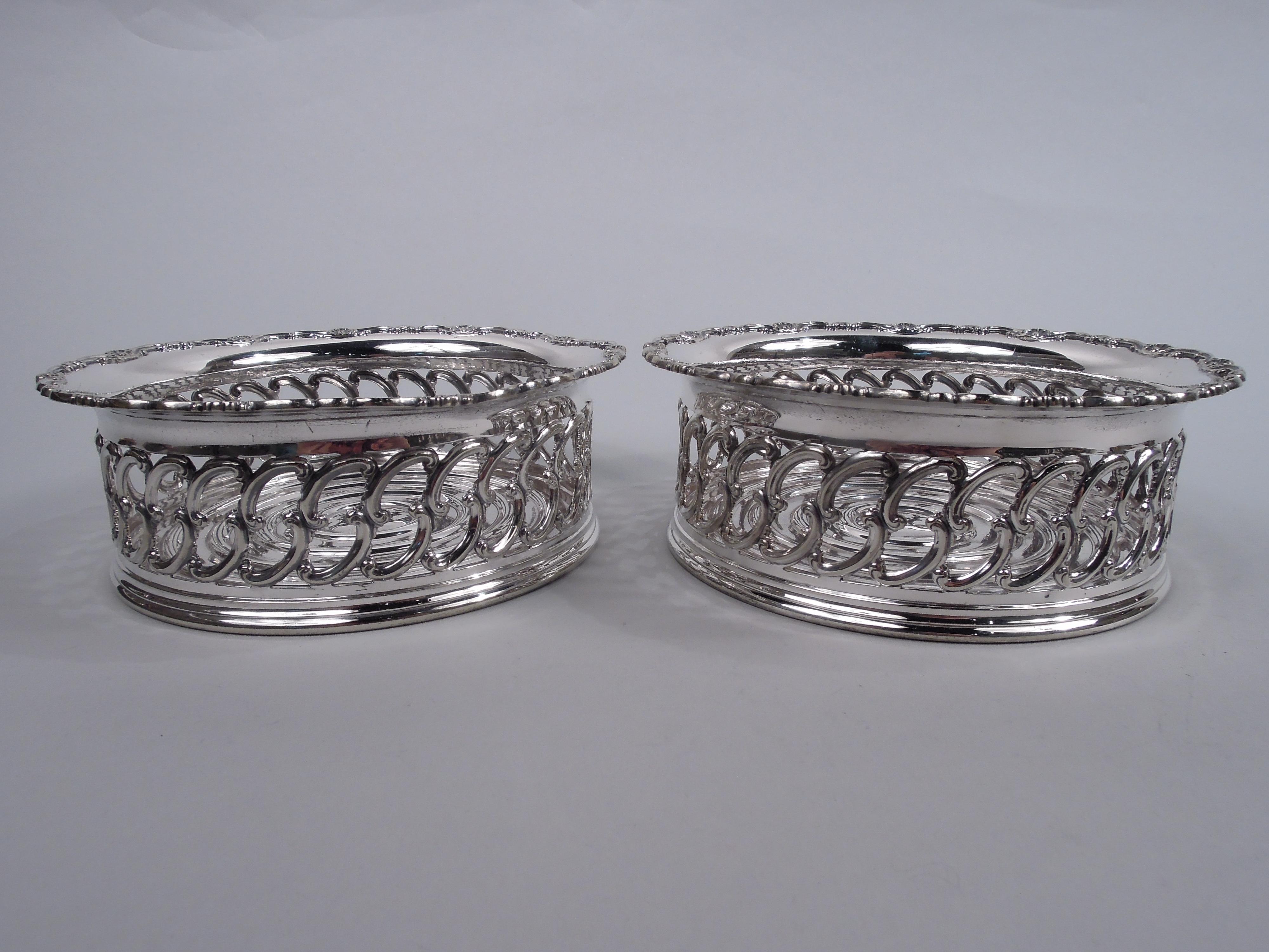 Pair of Edwardian Classical silver-plated wine bottle coasters. Made by Tiffany & Co. in New York. Each: Round well with concentric rings. Sides have open scrollwork. Flared rim with applied scrolls and scallop shells. Fully marked including maker’s