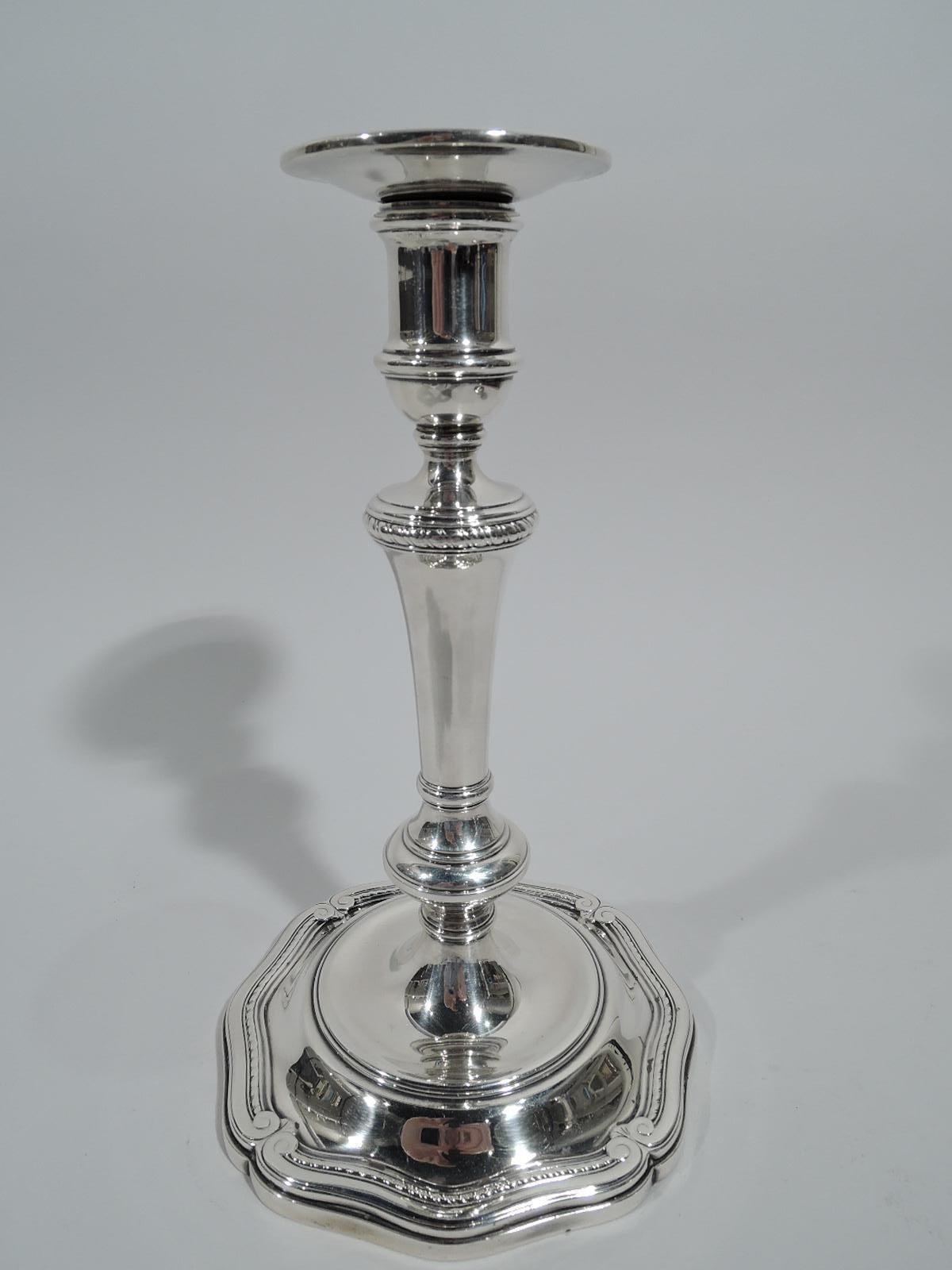Pair of Edwardian Classical sterling silver candlesticks. Made by Tiffany & Co. in New York, ca 1916. Spool socket on knopped and tapering shaft flowing into round base with concave well. Base rim has long and gentle scrolls with Classical volute