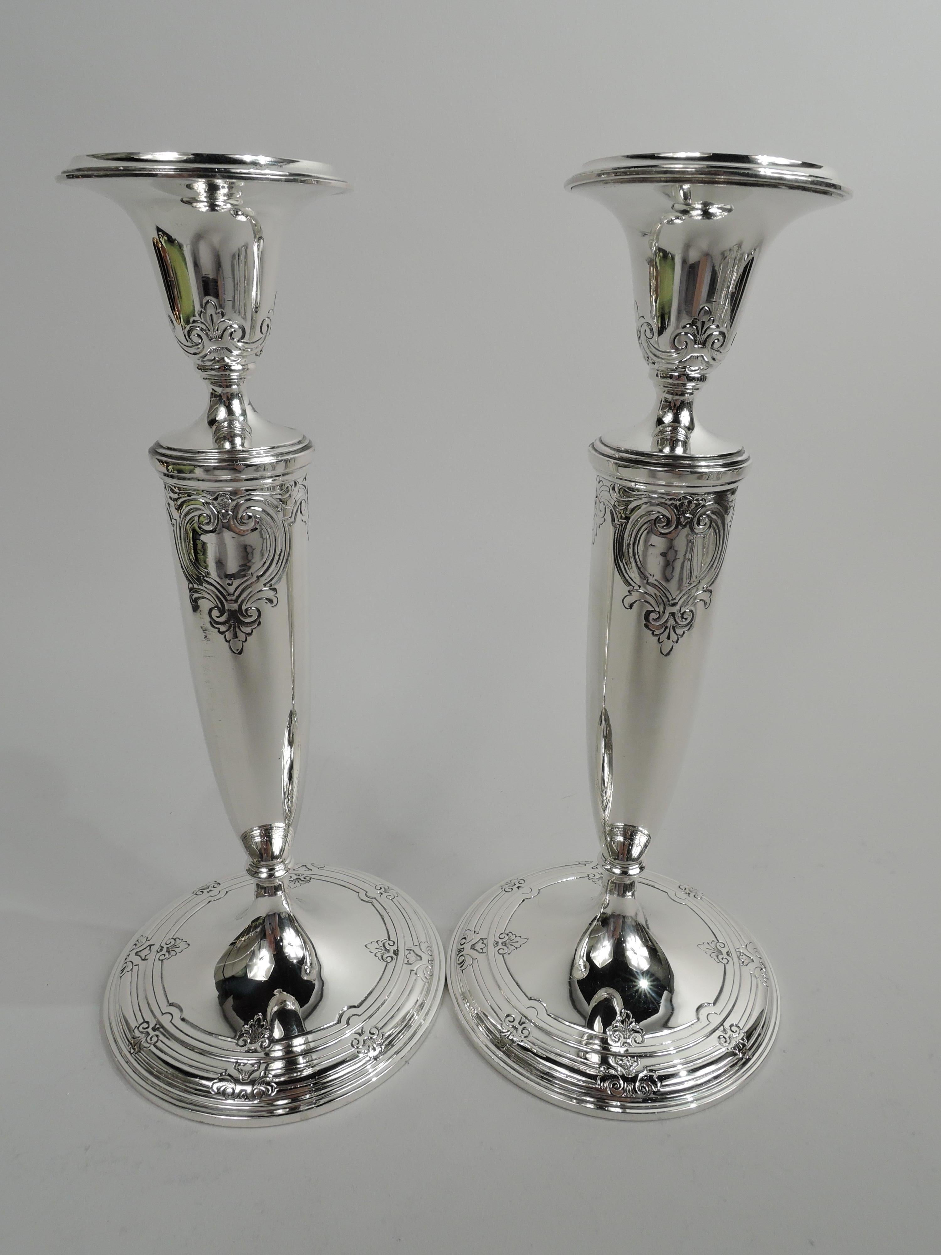 Pair of Edwardian Classical sterling silver candlesticks. Made by Tiffany & Co. in New York, ca 1922. Tapering socket with detachable bobeche on tapering shaft with base knop and raised foot. Chased leafing scrollwork and two cartouches of which one