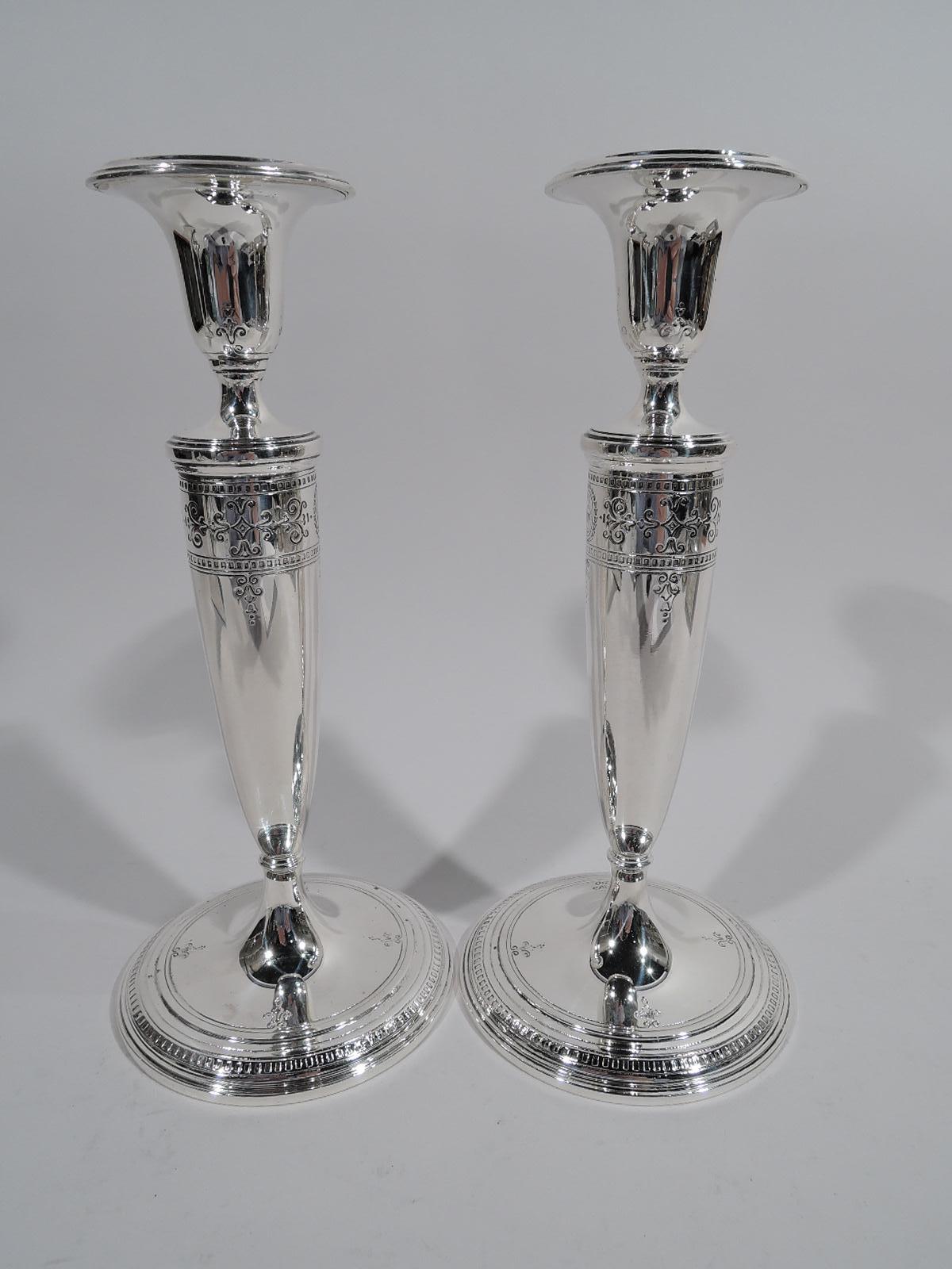 Pair of Edwardian Regency sterling silver candlesticks. Made by Tiffany & Co. in New York, circa 1922. Urn socket with detachable bobeche, tapering shaft, and raised and stepped foot. Engraved ornament on shaft top: scrollwork and wreaths inset with