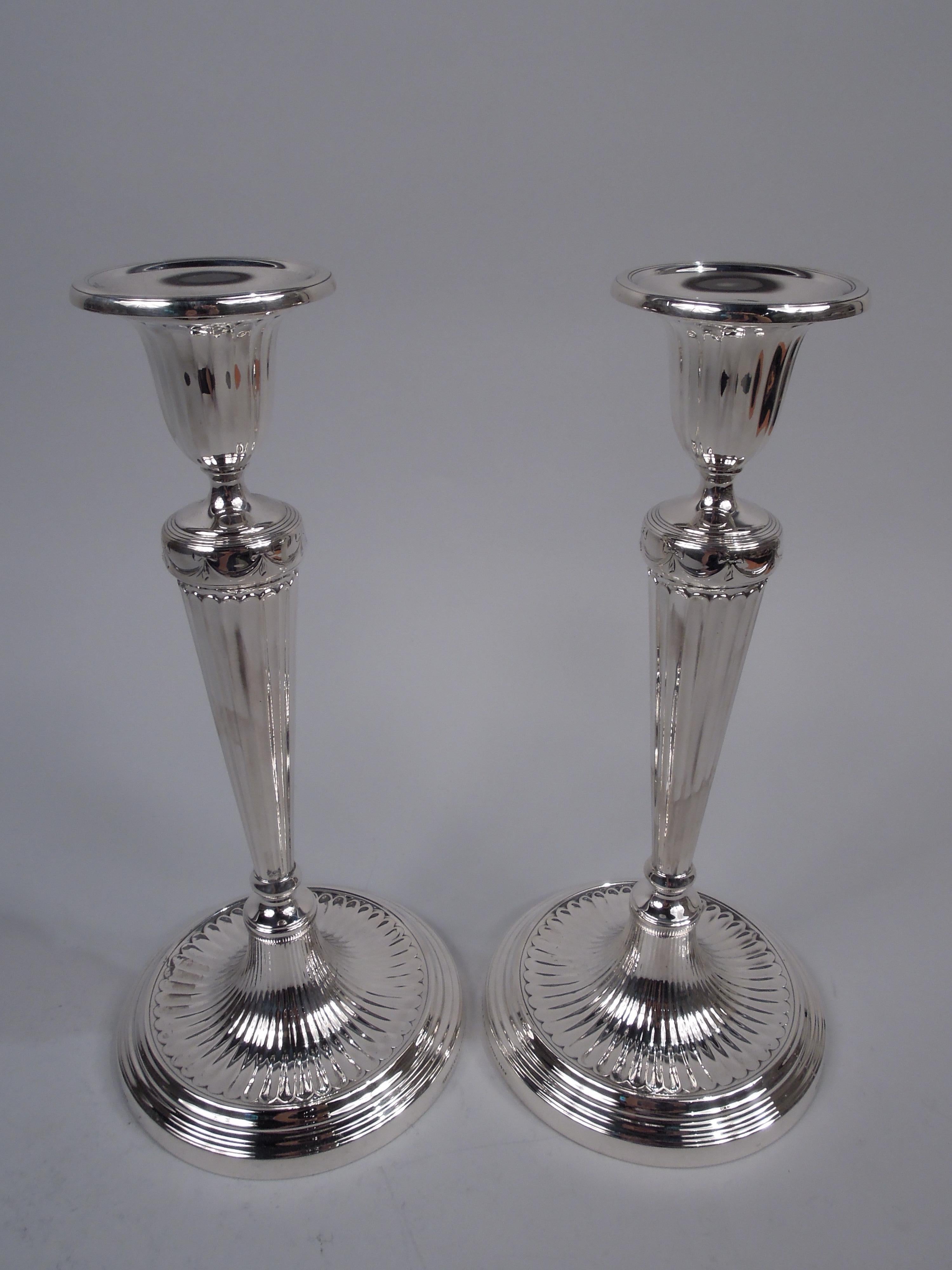 Pair of English Neoclassical sterling silver candlesticks. Made by Tiffany & Co. in New York, ca 1916. Each: Tapering column on dome flowing into stepped and concave base. Tapering socket with detachable bobeche. Ribboned swags. Fine fluting that
