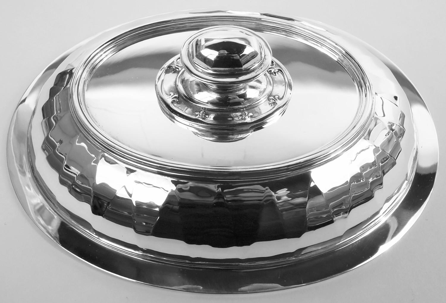 Pair of Saint Dunstan sterling silver covered vegetable dishes. Made by Tiffany & Co. in New York, ca 1910. Each: Oval and tapering bowl; cover domed. Trefoil rims on bowl and cover interior as well as bordering twist-lock handle. Faceting. A