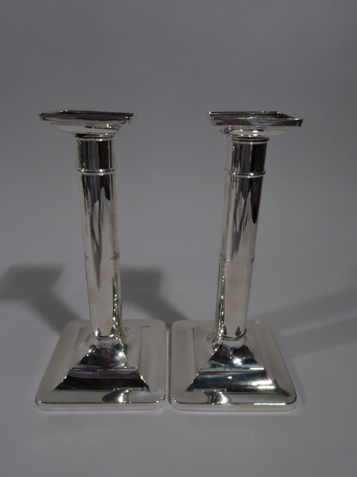 Pair of sterling silver candlesticks. Made by Tiffany & Co. in New York, circa 1910. Column shaft with knop at base; foot square and stepped; bobéches square and detachable. Spare Classicism with engraved strap work armorial cartouche (vacant).