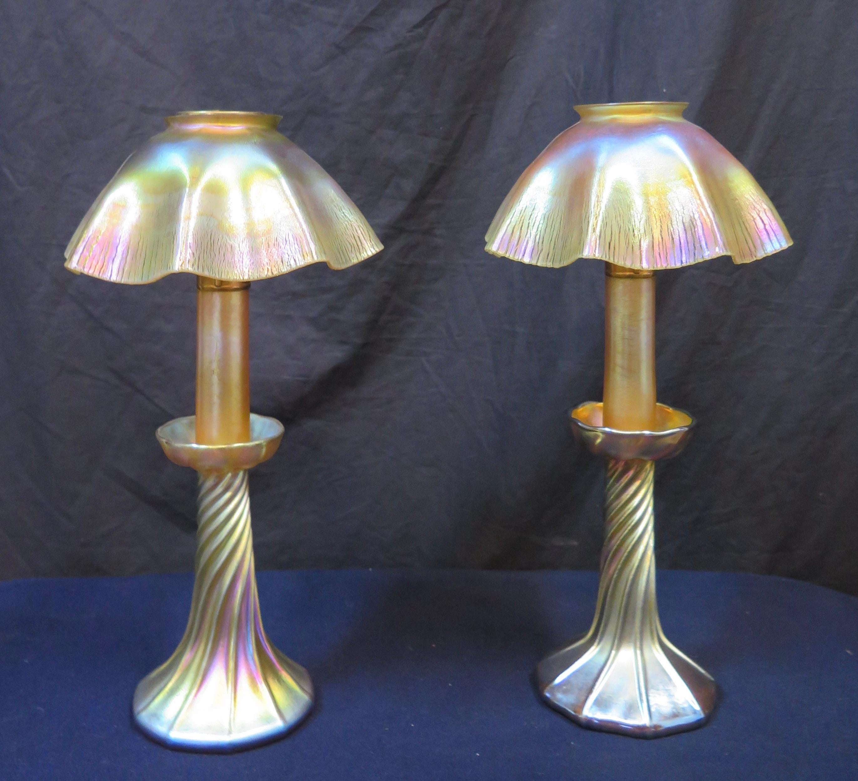 This wonderful pair of original authentic Tiffany Studios favrile art glass candlestick lamps date from the early 20th century. Each hand blown lamp is decorated with original pleated iridescent favrile shades supported on kerosene candle holders